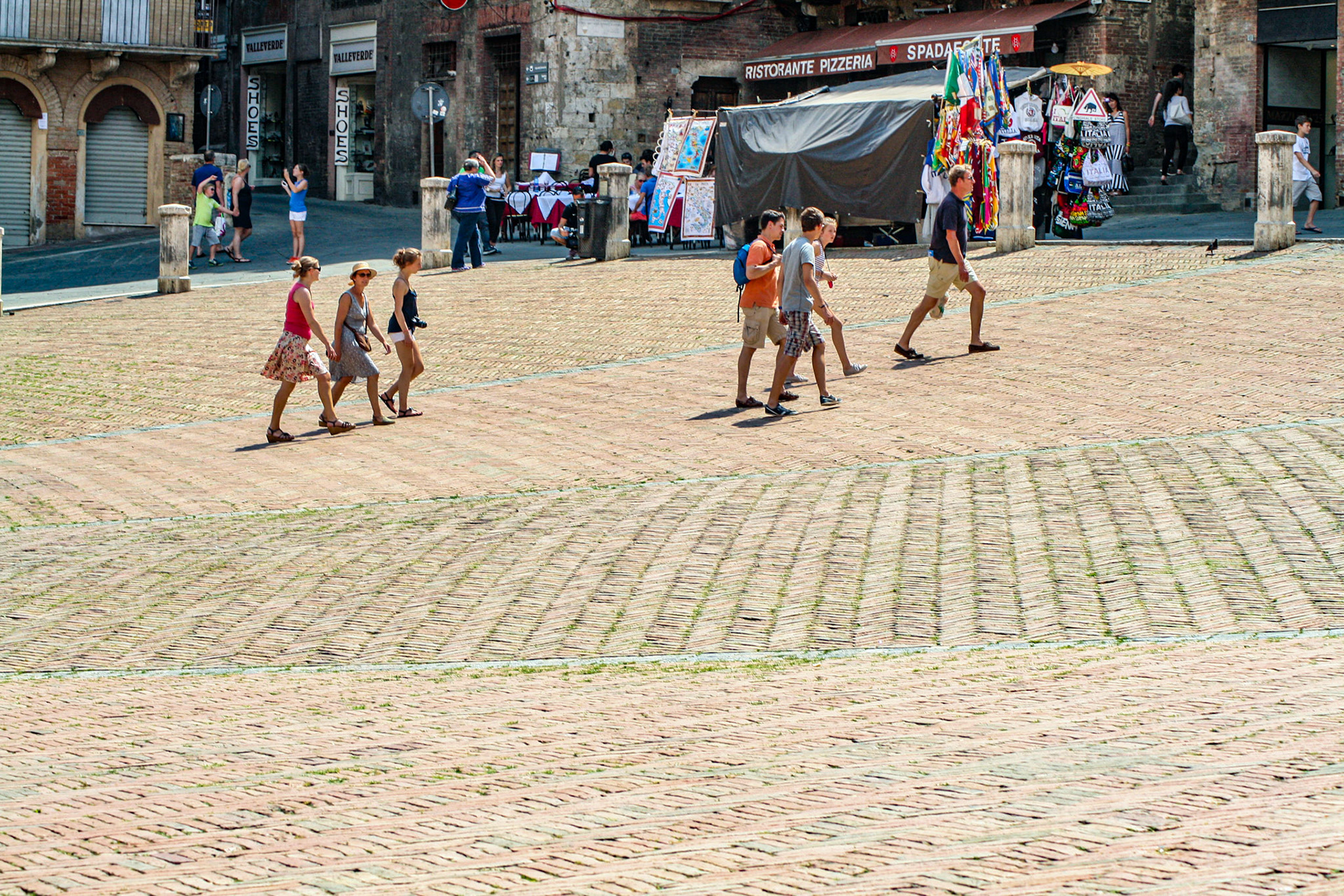 The Piazza del Campo was paved in 1349 in fishbone-patterned red brick with 8 lines of travertine, which divide the piazza into 9 sections, radiating from the mouth of the gavinone (the central water drain) in front of the Palazzo Pubblico. The number of divisions is held to be symbolic of the rule of The Nine (Noveschi) who laid out the campo and governed Siena at the height of its mediaeval splendor between 1292-1355. The Campo was and remains the focal point of public life in the city. From the piazza, eleven narrow shaded streets radiate into the city. 