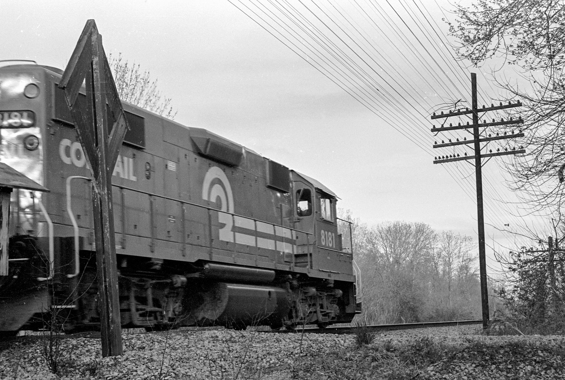 An eastbound crosses the dirt road crossing protected by a steam-era crossbuck.