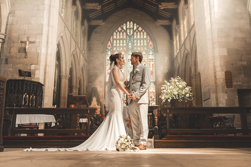 Natalia and Daniel share a joyful moment outside St James's Church in Louth immediately after their wedding ceremony, surrounded by historic stone architecture on a glorious sunny day.