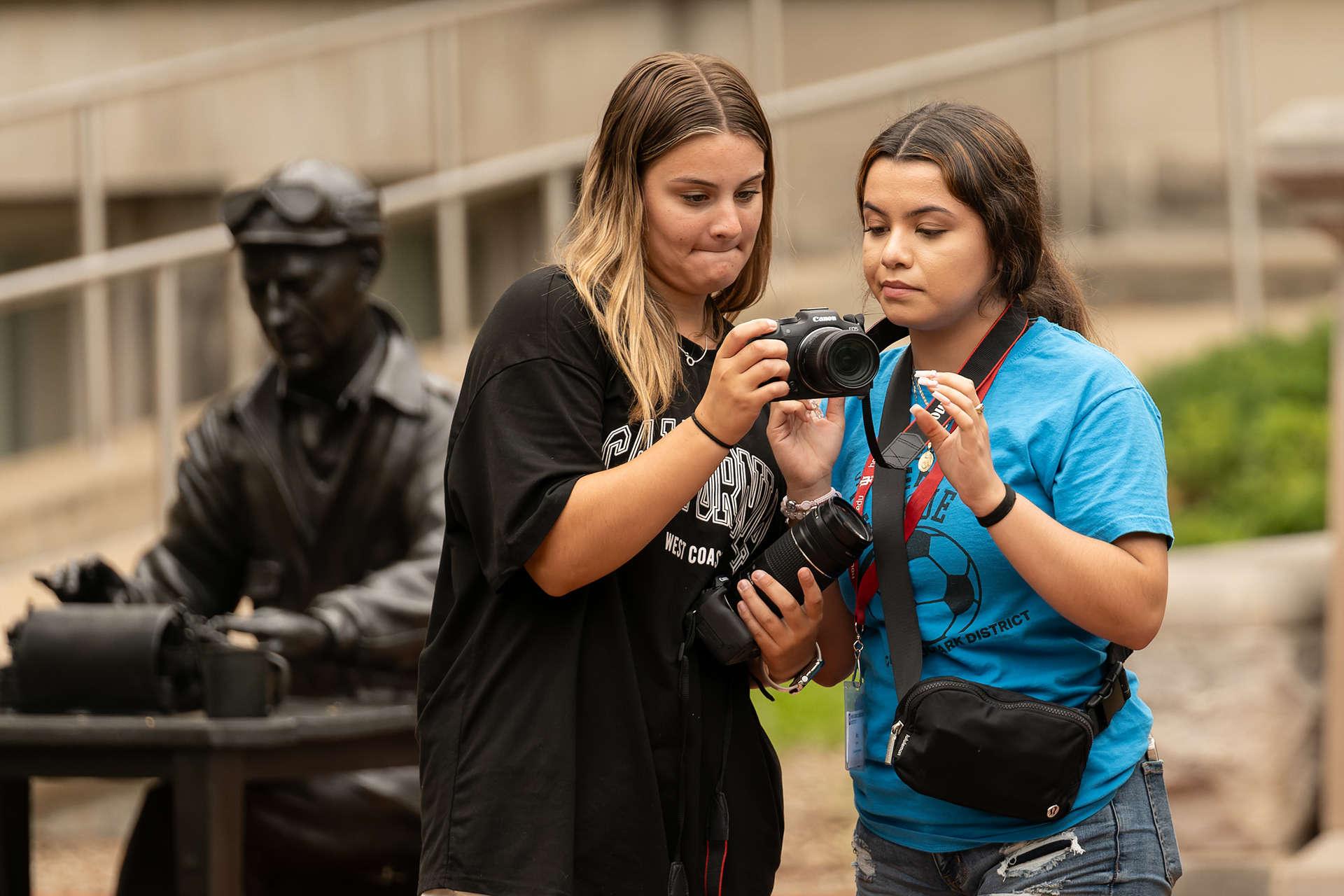 Students use their cameras in front of Franklin Hall during the first day of the Indiana University High School Journalism Institute, Monday, July 8, 2024, in Bloomington, Ind. A sculpture of IU alumnus and World War II correspondent Ernie Pyle sits behind. (Vincent Hsiao/HSJI)