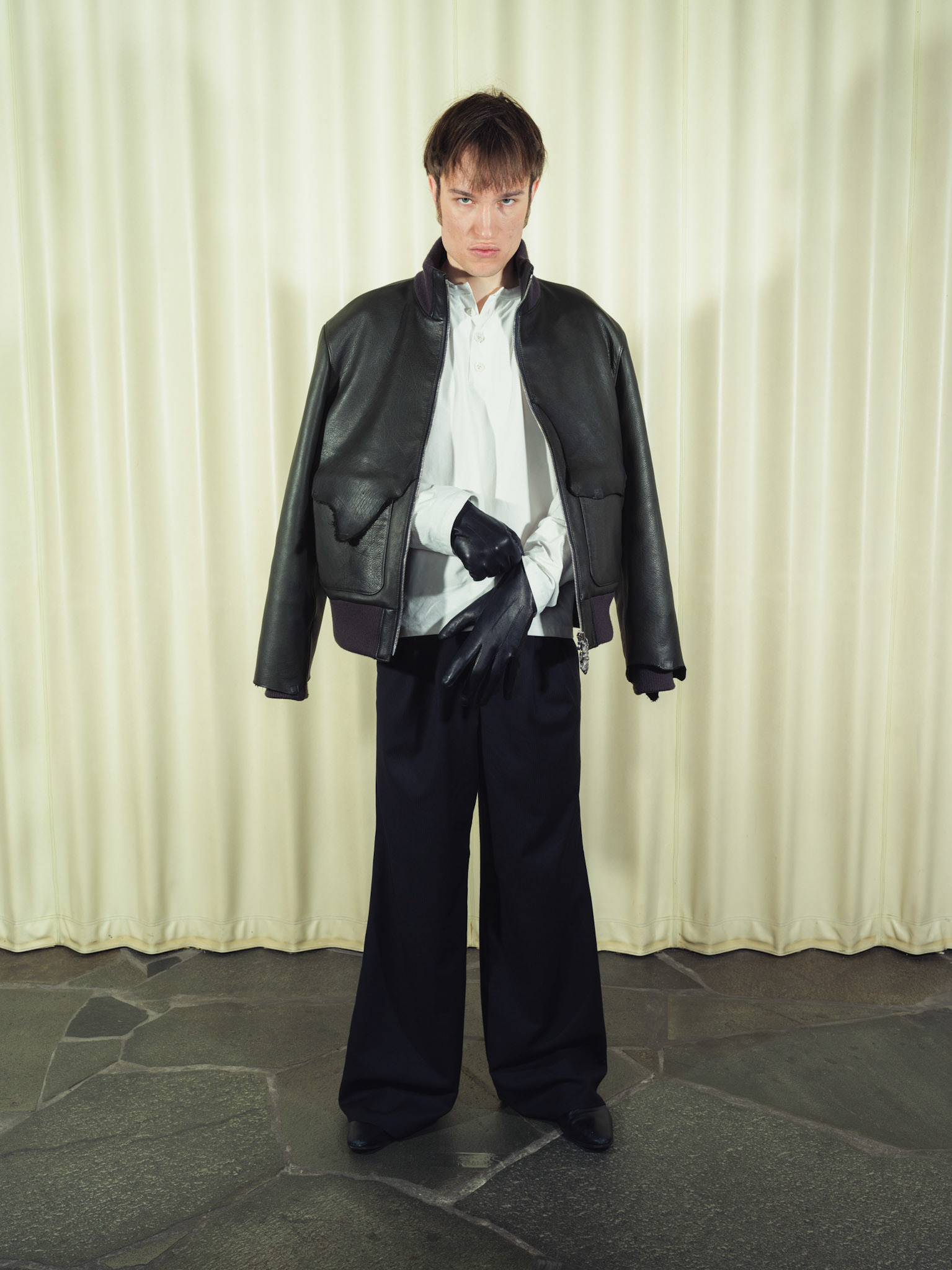 Raw edge calfskin leather jacket with handmade silver zipper tabs, Cotton poplin henley shirt with handmade ceramic buttons, Pleated wide-leg pinstripe wool trousers