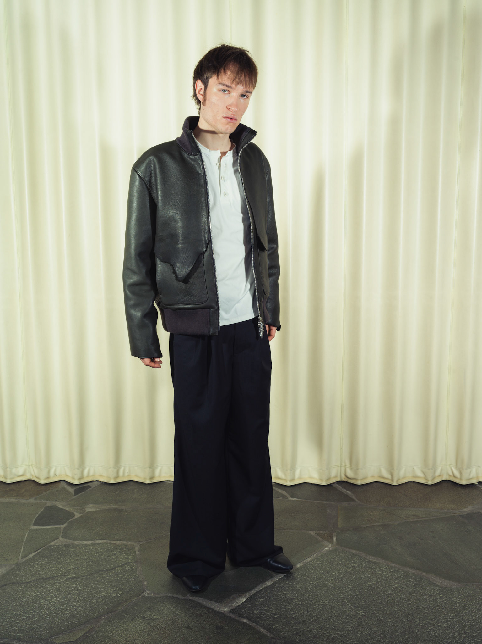 Raw edge calfskin leather jacket with handmade silver zipper tabs, Cotton poplin henley shirt with handmade ceramic buttons, Pleated wide-leg pinstripe wool trousers