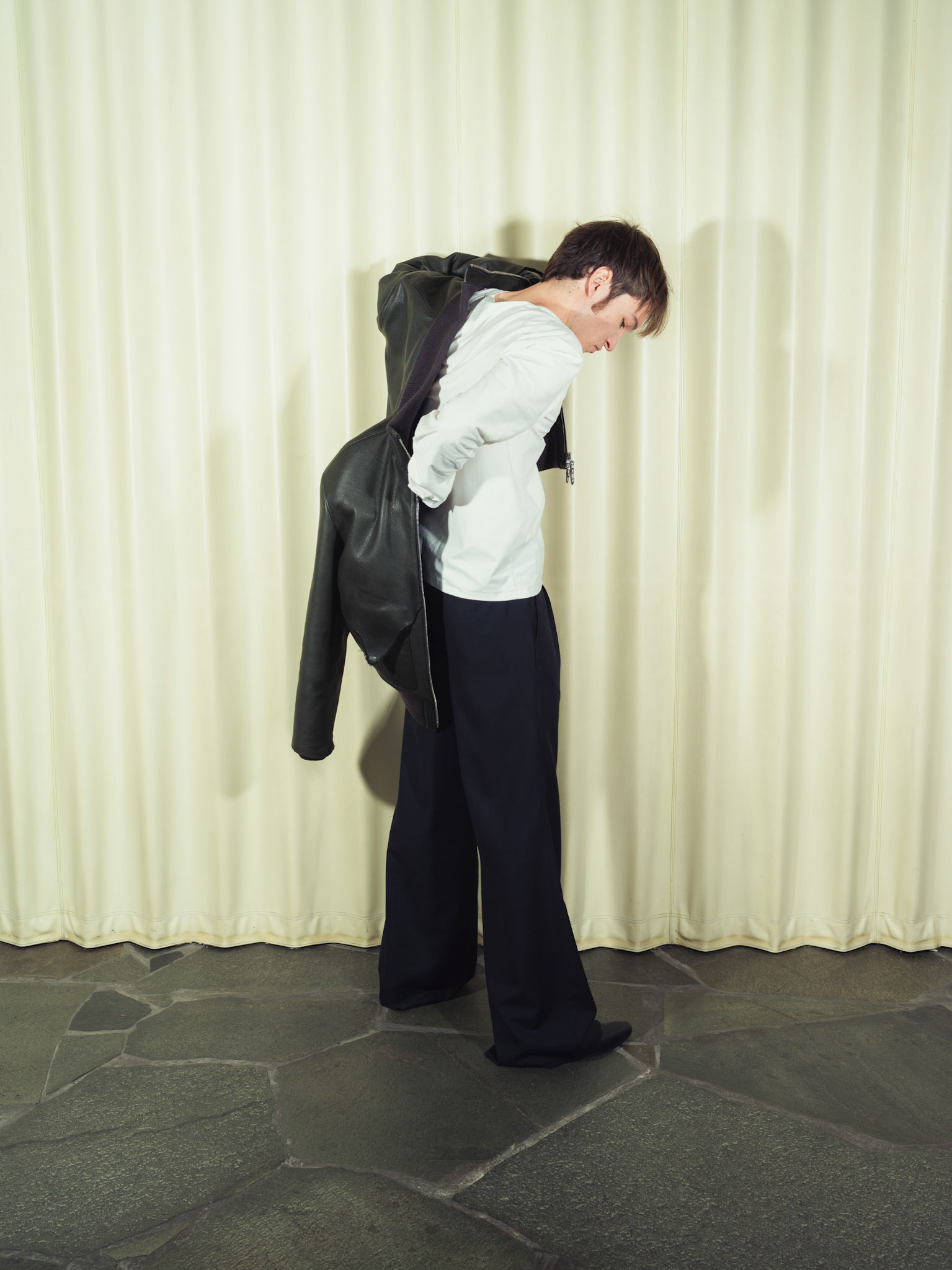 Raw edge calfskin leather jacket with handmade silver zipper tabs, Cotton poplin henley shirt with handmade ceramic buttons, Pleated wide-leg pinstripe wool trousers