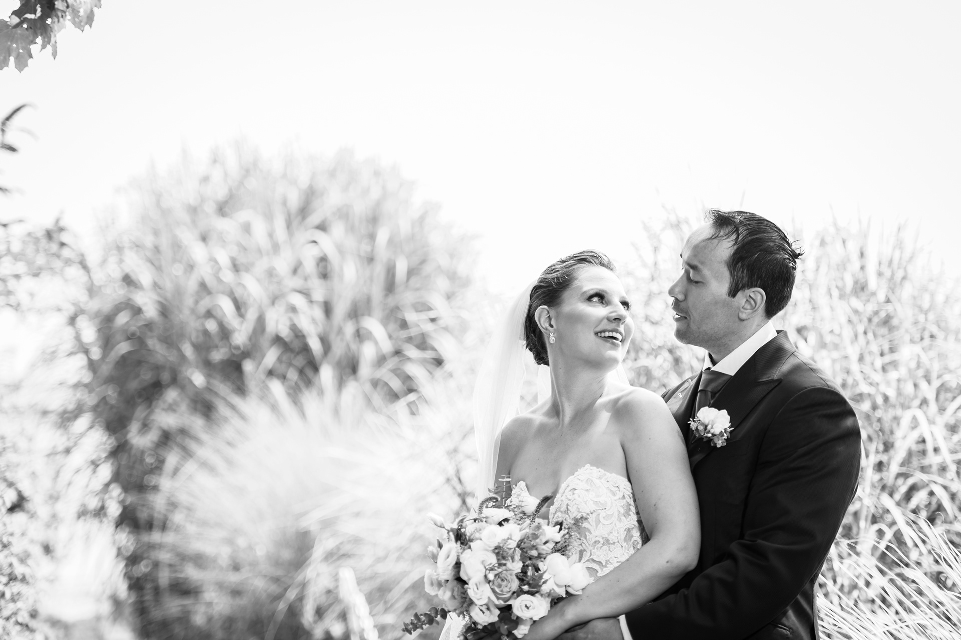Black and white portrait of couple outdoors, bride holding bouquet.