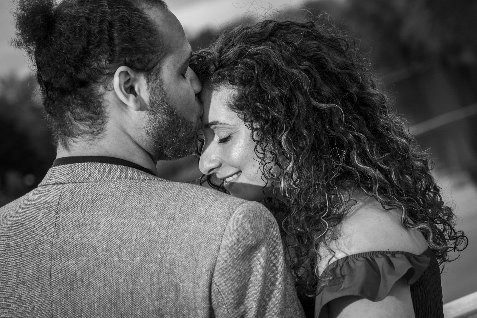 Black and white engagement portrait of a couple sharing a tender forehead kiss.