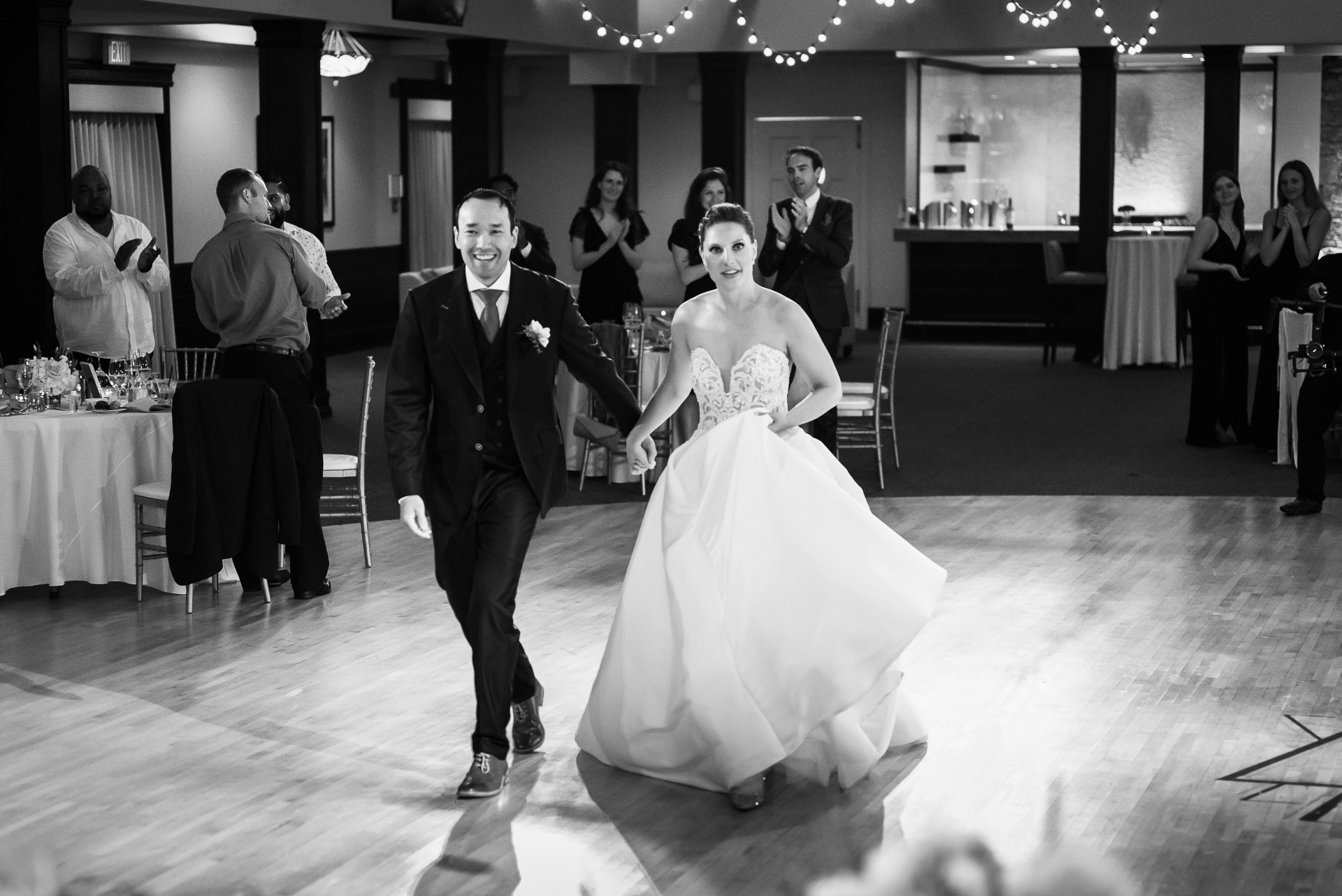 Bride and groom walking hand in hand into the reception as guests applaud.