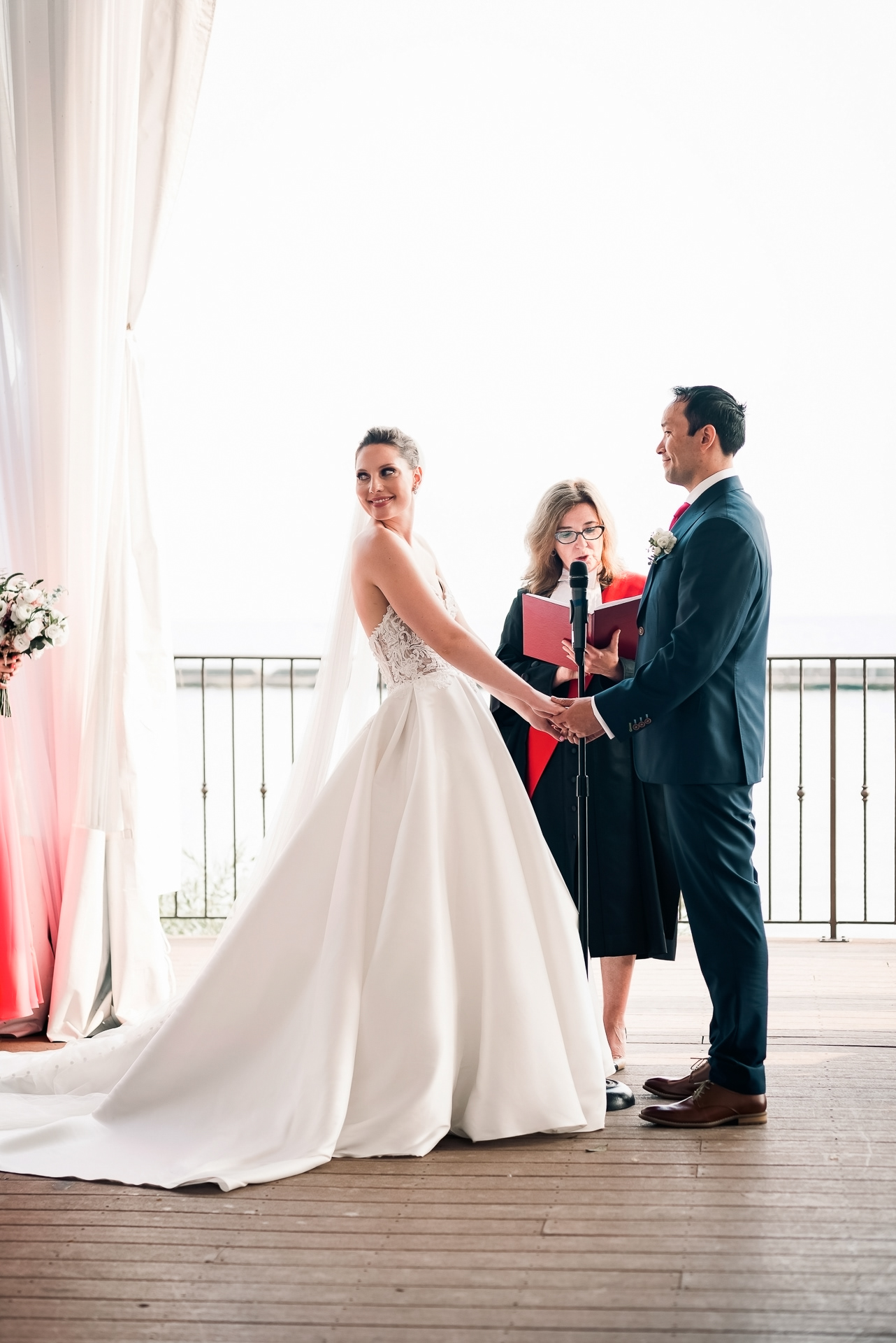 Bride smiling at the officiant while holding hands with the groom on the Palais Royale terrace.