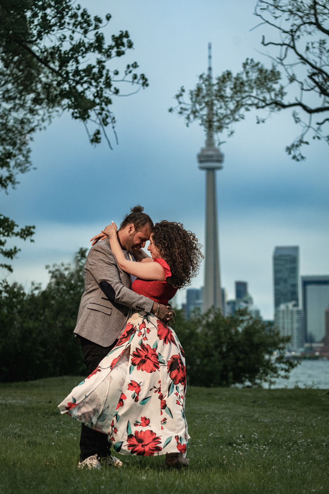 Romantic engagement photo of a couple embracing in front of Toronto skyline at sunset.