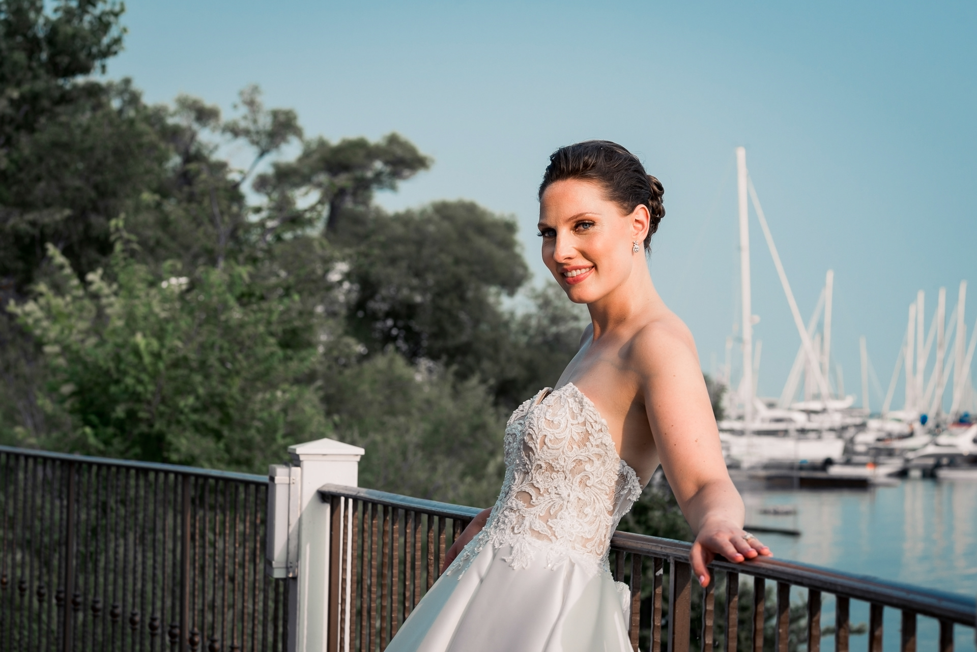 Bride posing by the marina railing, elegant lace detail on gown.