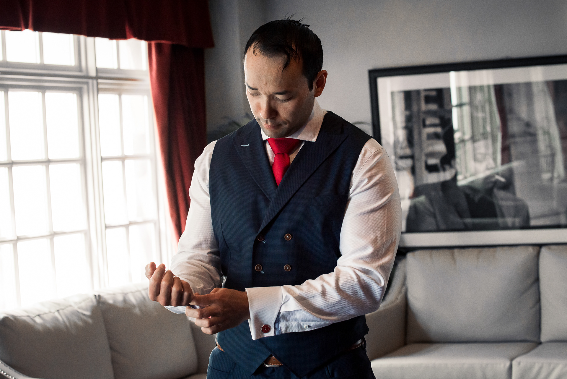 Groom adjusting his sleeve with red tie showing.