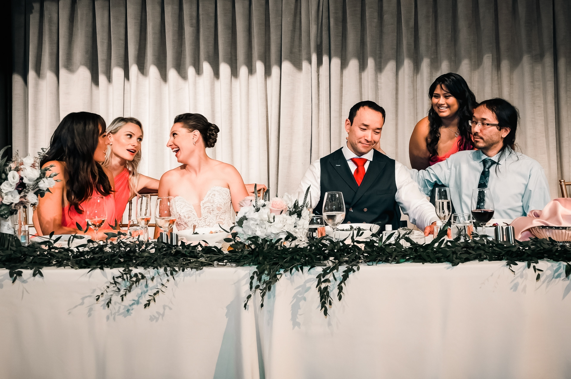 Bride, groom, and wedding party laughing together at the head table.