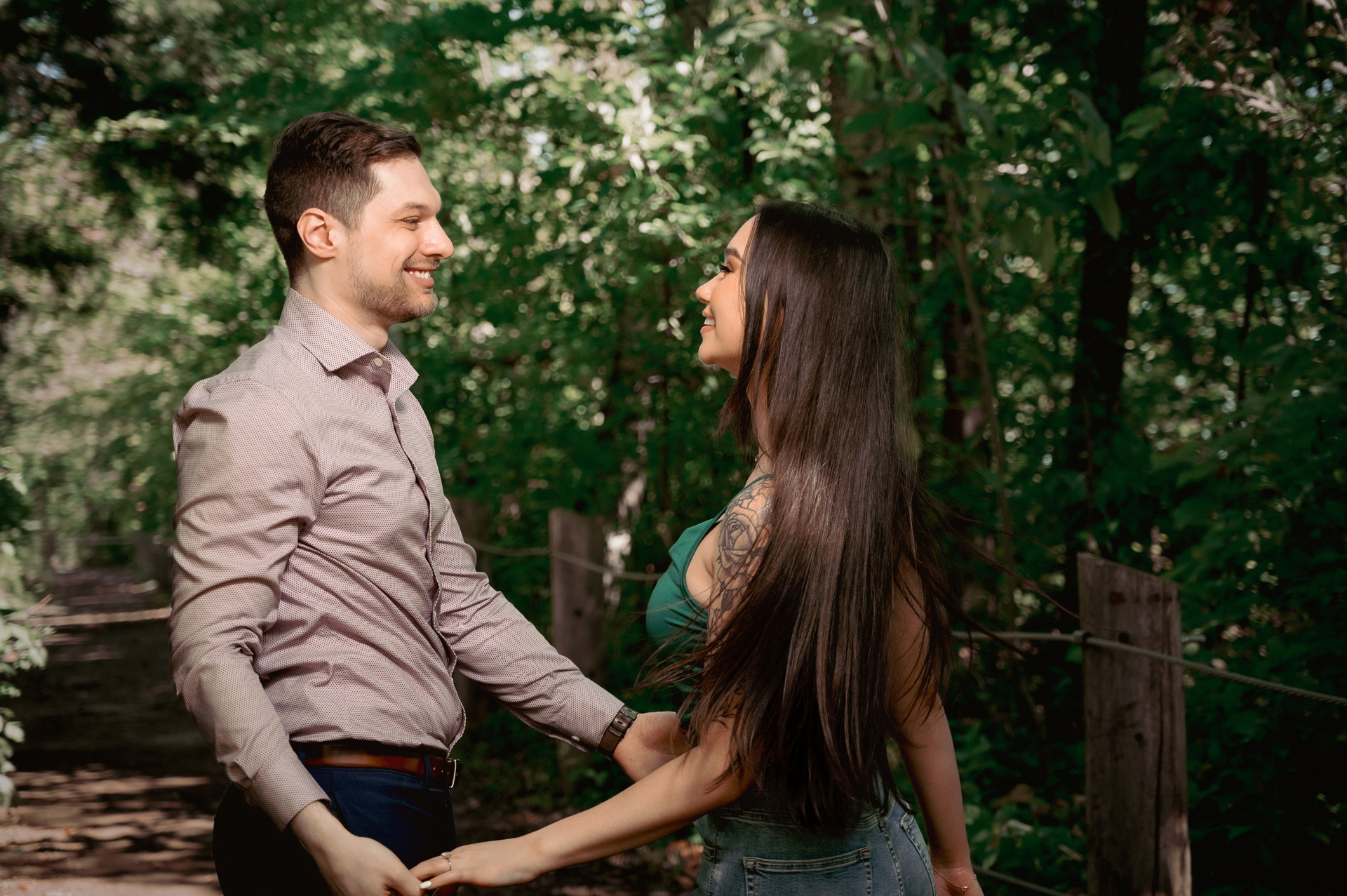 Couple holding hands in a wooded path, gazing at each other lovingly.