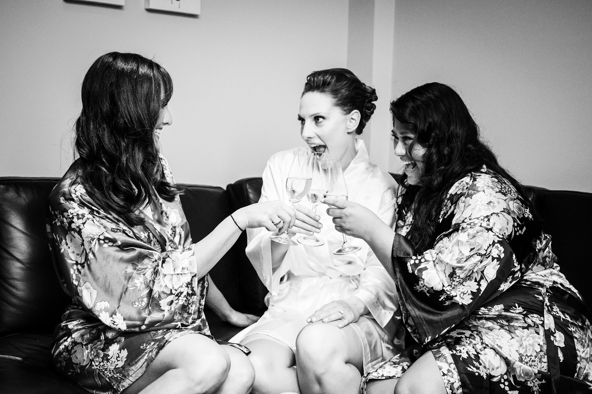 Bridesmaids in robes cheering with bride during morning prep.