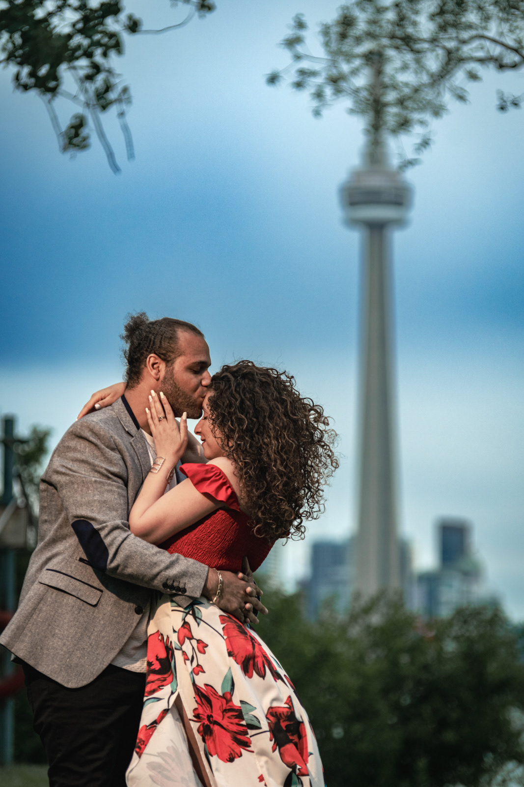 ouple kissing in front of CN Tower and Toronto skyline during their engagement session.