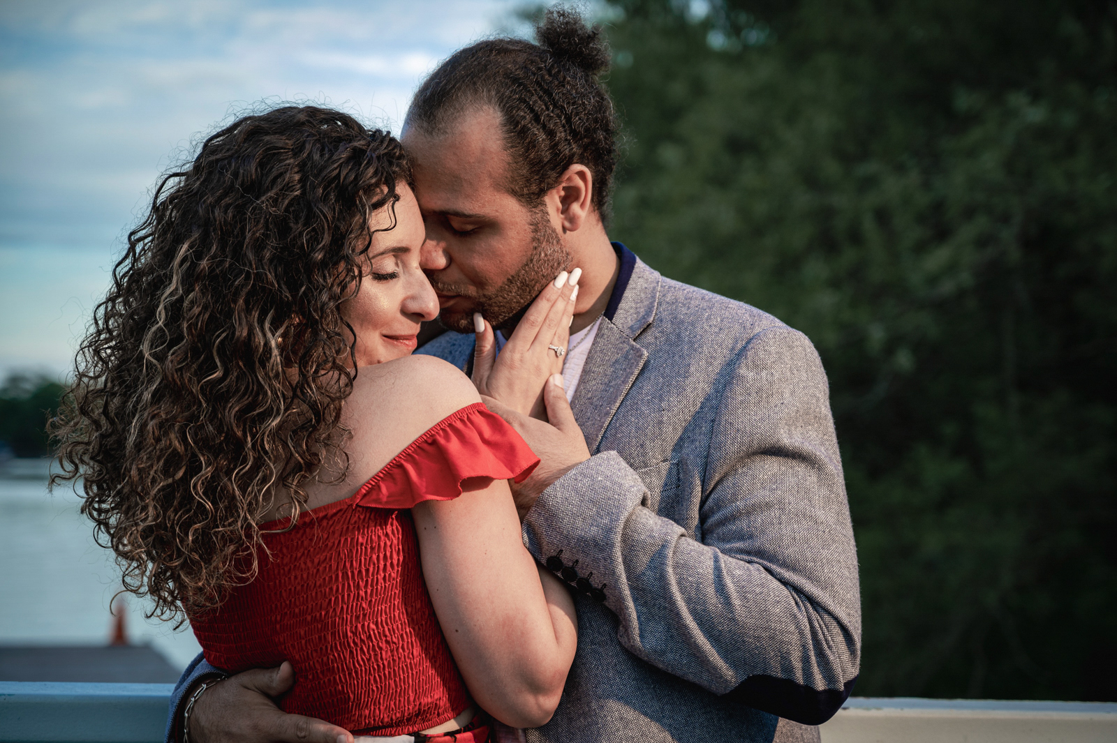 Romantic close-up of bride-to-be touching her fiancé’s face with engagement ring on display.