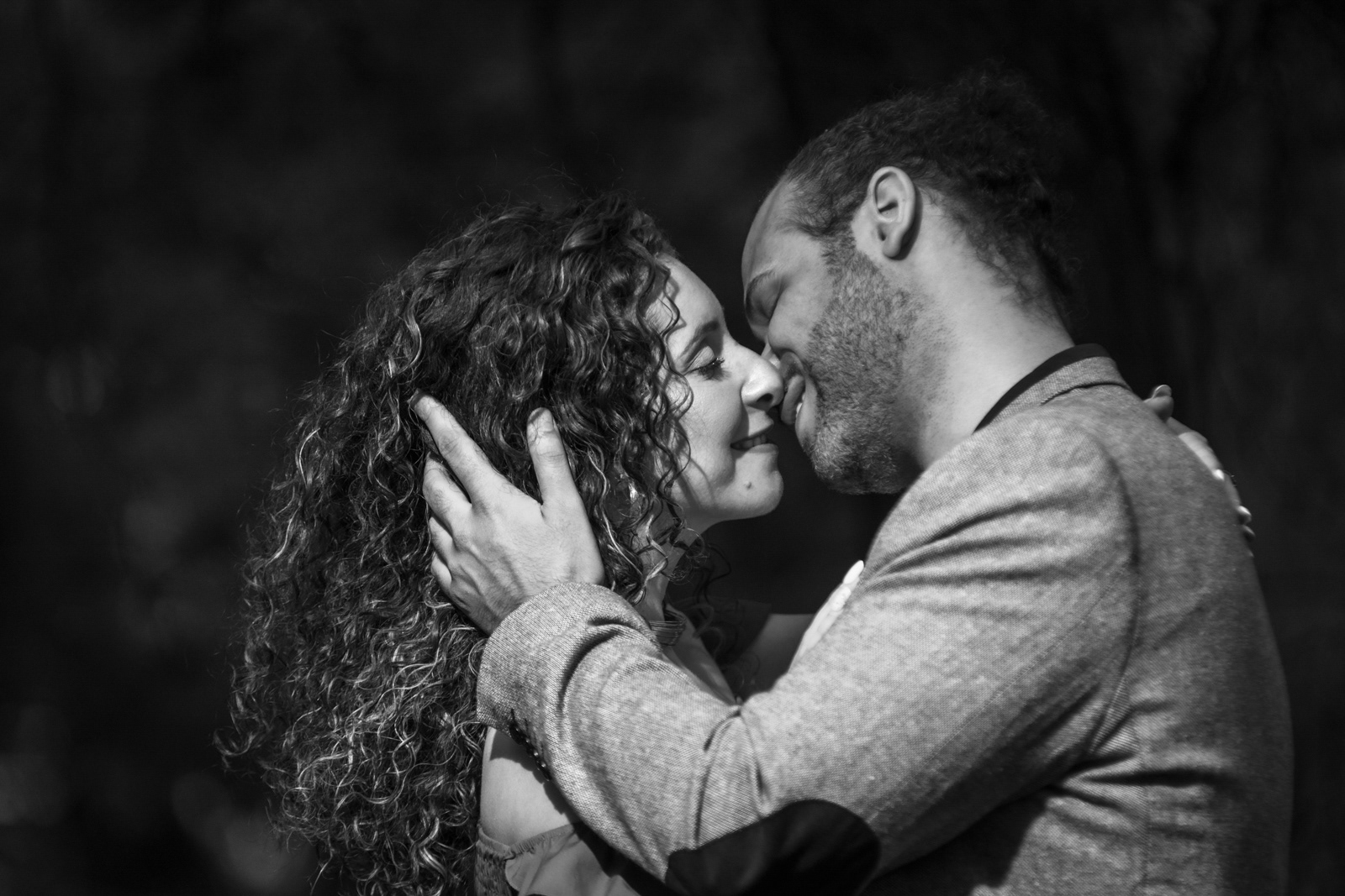 Black and white photo of engaged couple sharing a kiss in the park.