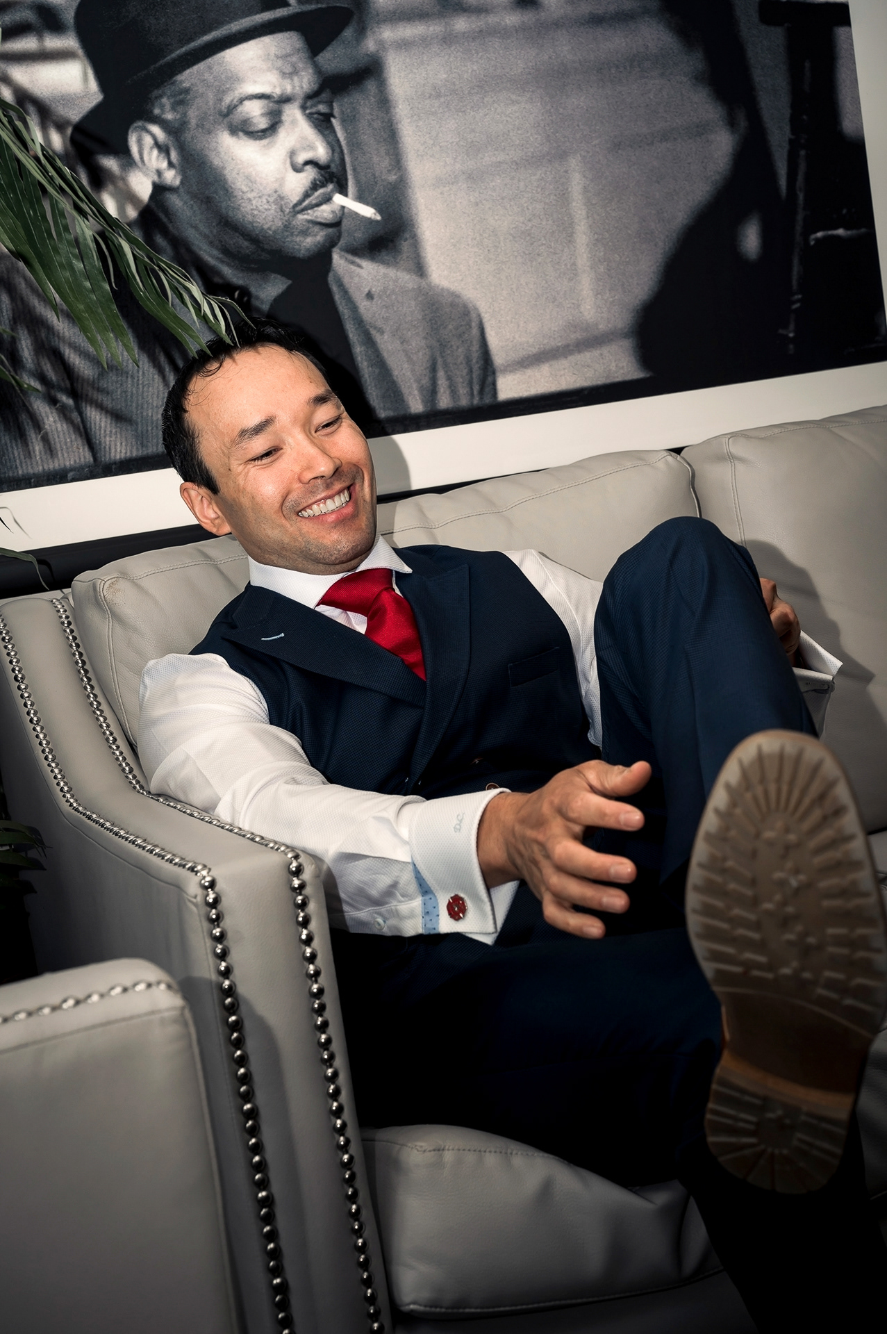 Groom laughing while relaxing on a couch in hotel suite.