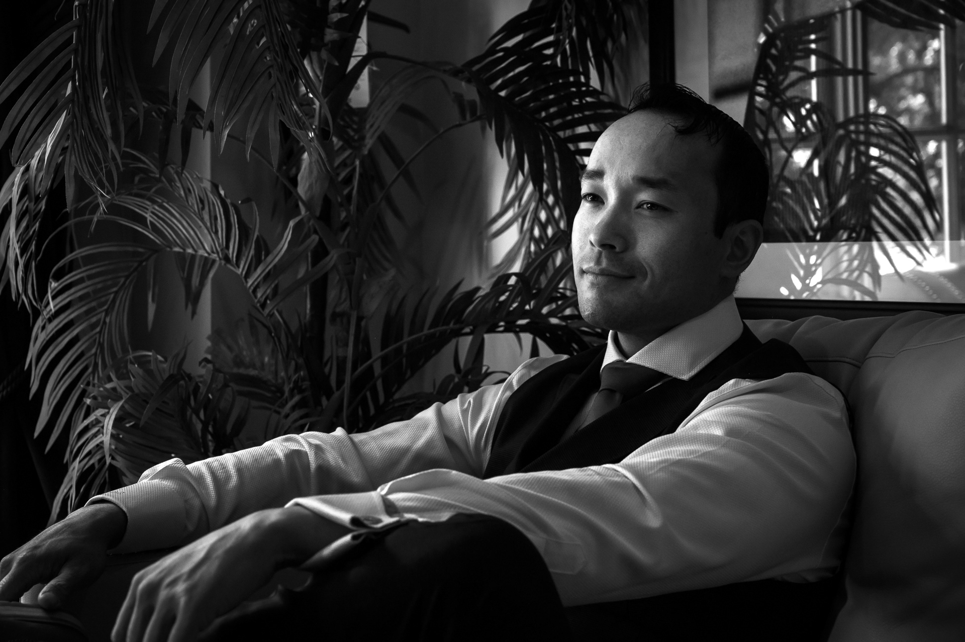 Black and white portrait of groom sitting by a plant before the ceremony.