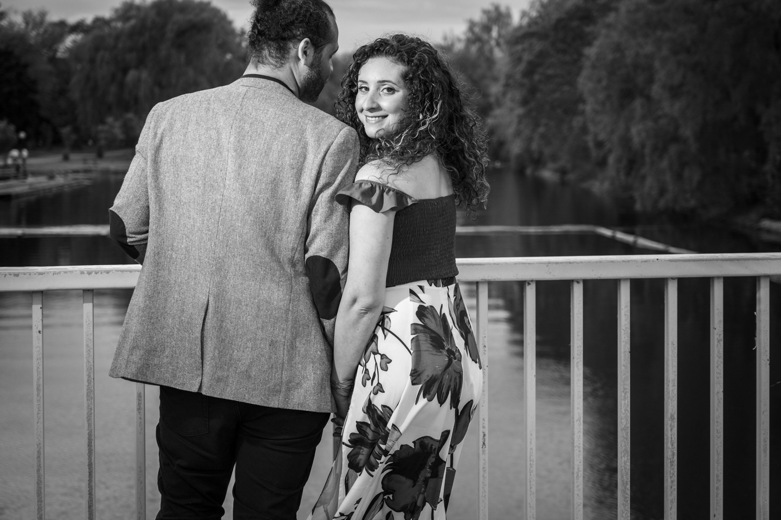 Bride-to-be looking back playfully at the camera while holding her fiancé’s hand on a bridge.