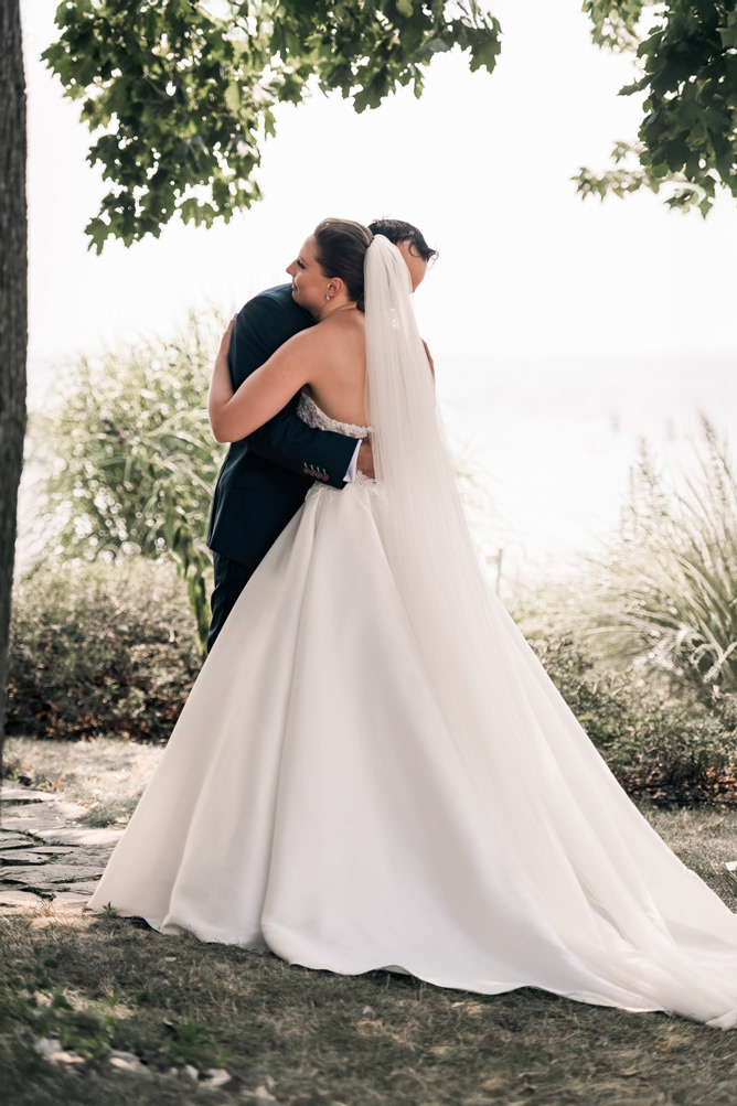 Bride embracing groom in garden near the waterfront.