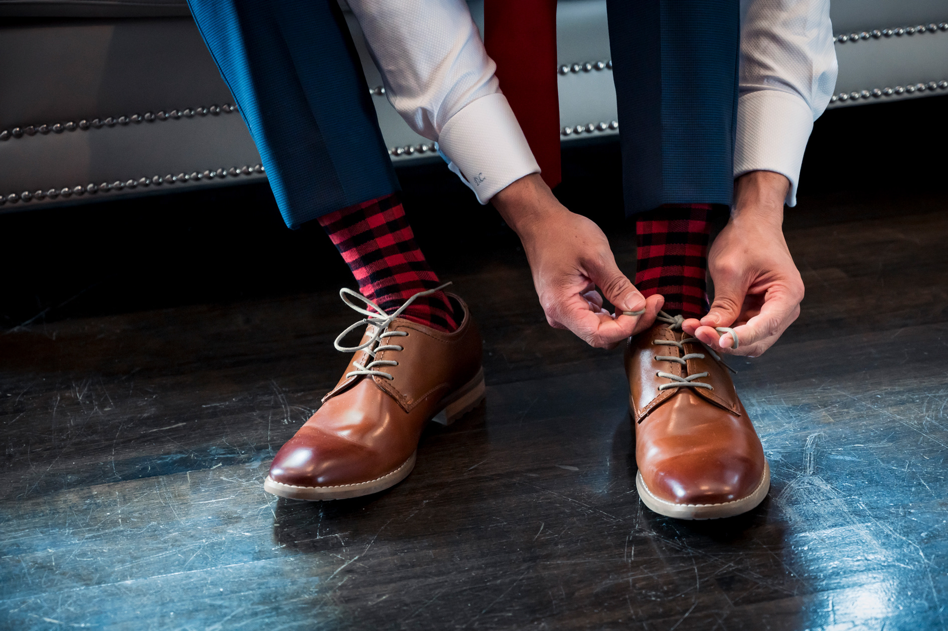 Close-up of groom tying shoelaces on polished brown leather shoes.