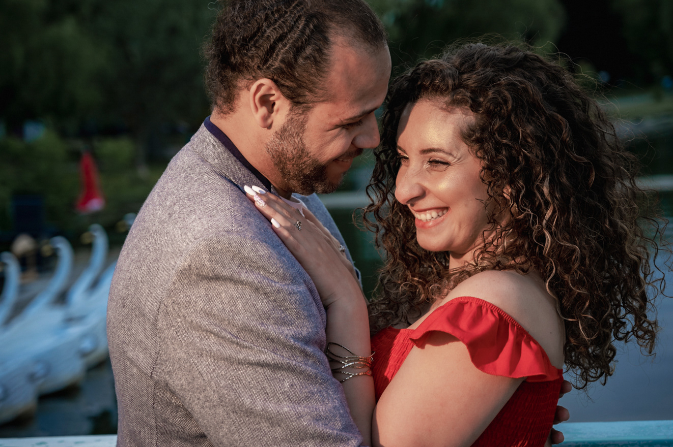Romantic engagement photo of a smiling couple holding each other outdoors at sunset.