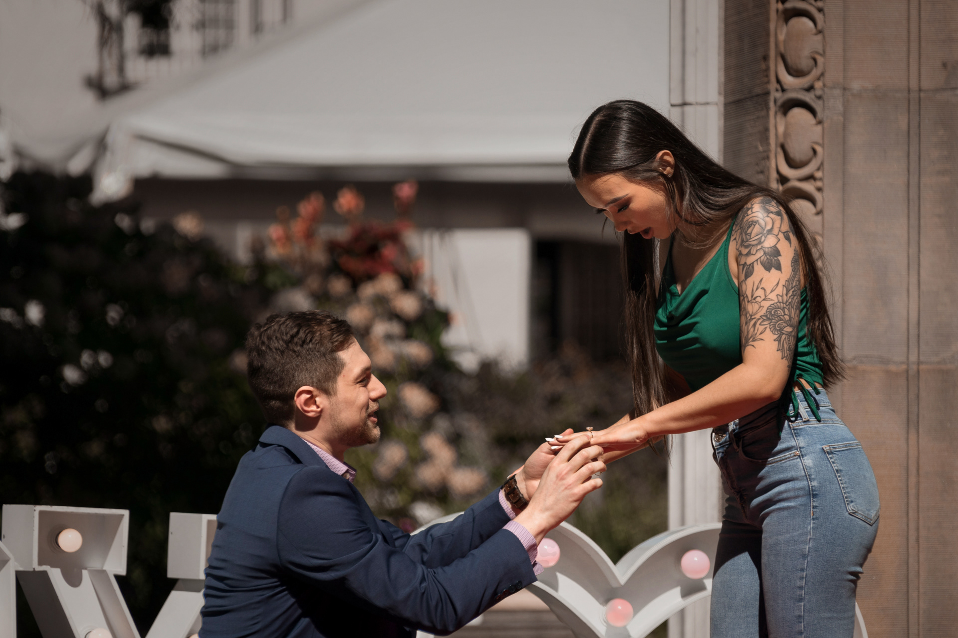 Groom-to-be on one knee, sliding the ring on fiancée’s finger during proposal.