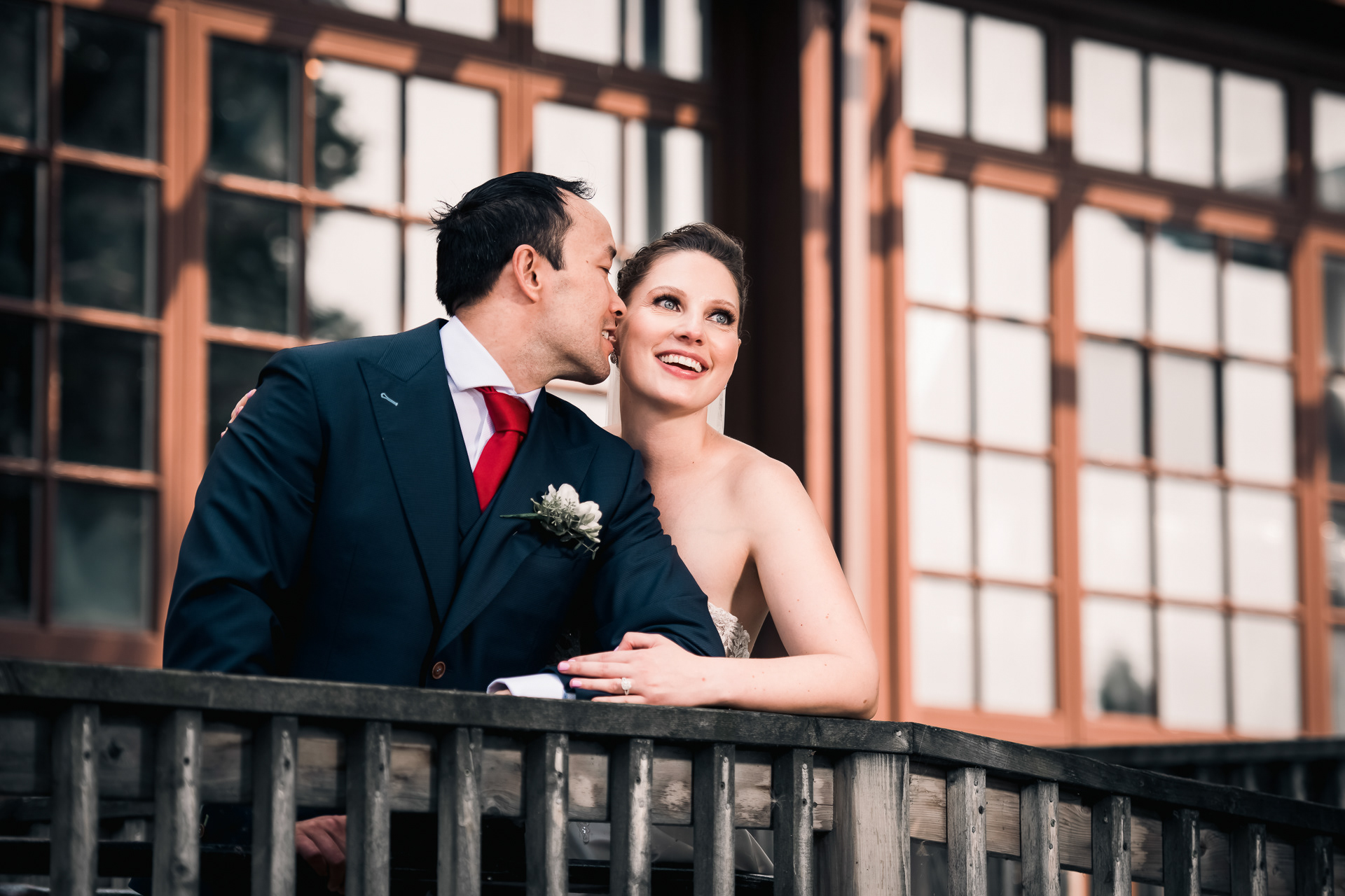 Groom kissing bride’s cheek as they share a quiet moment on the balcony.