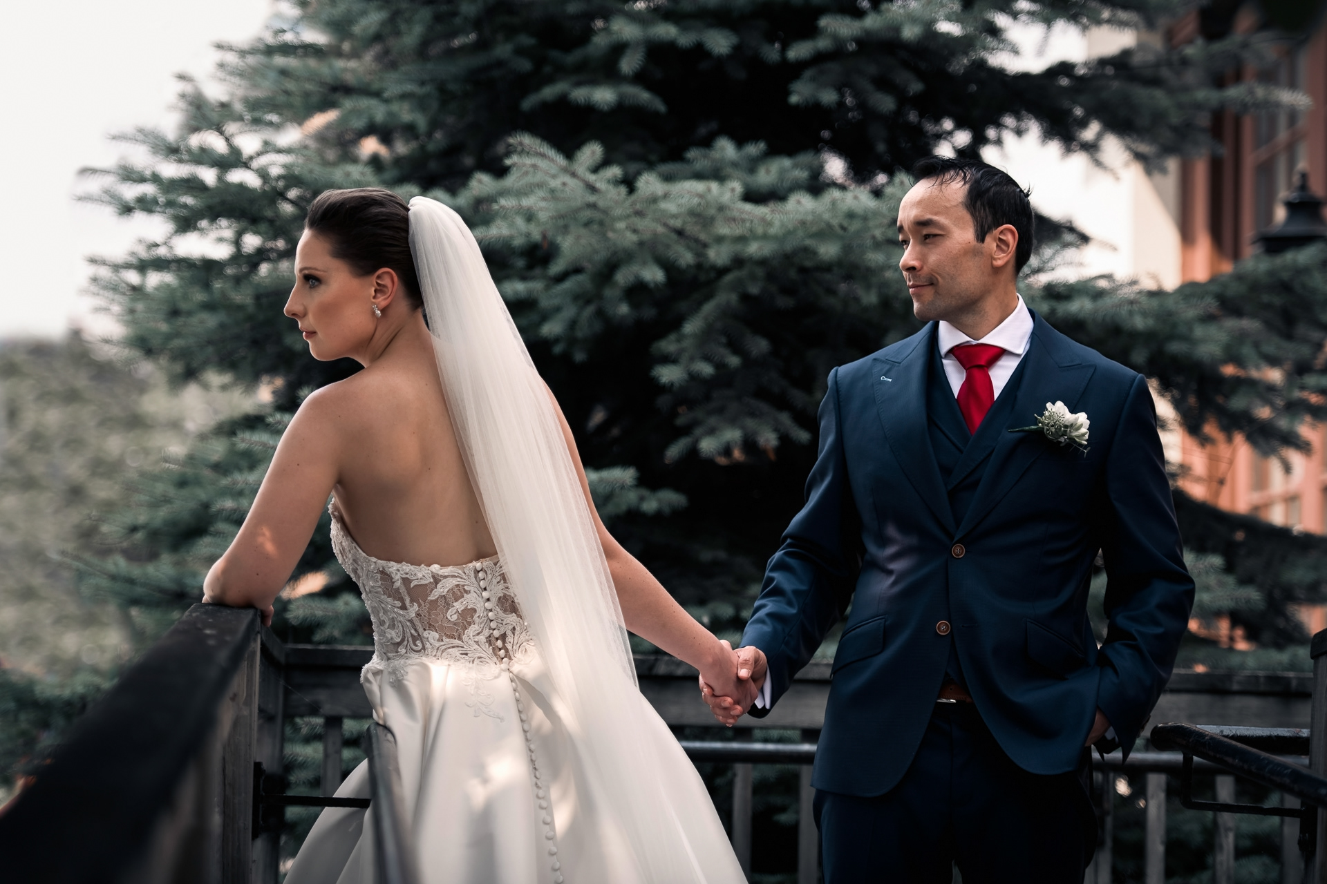Bride and groom holding hands outdoors against lush greenery.