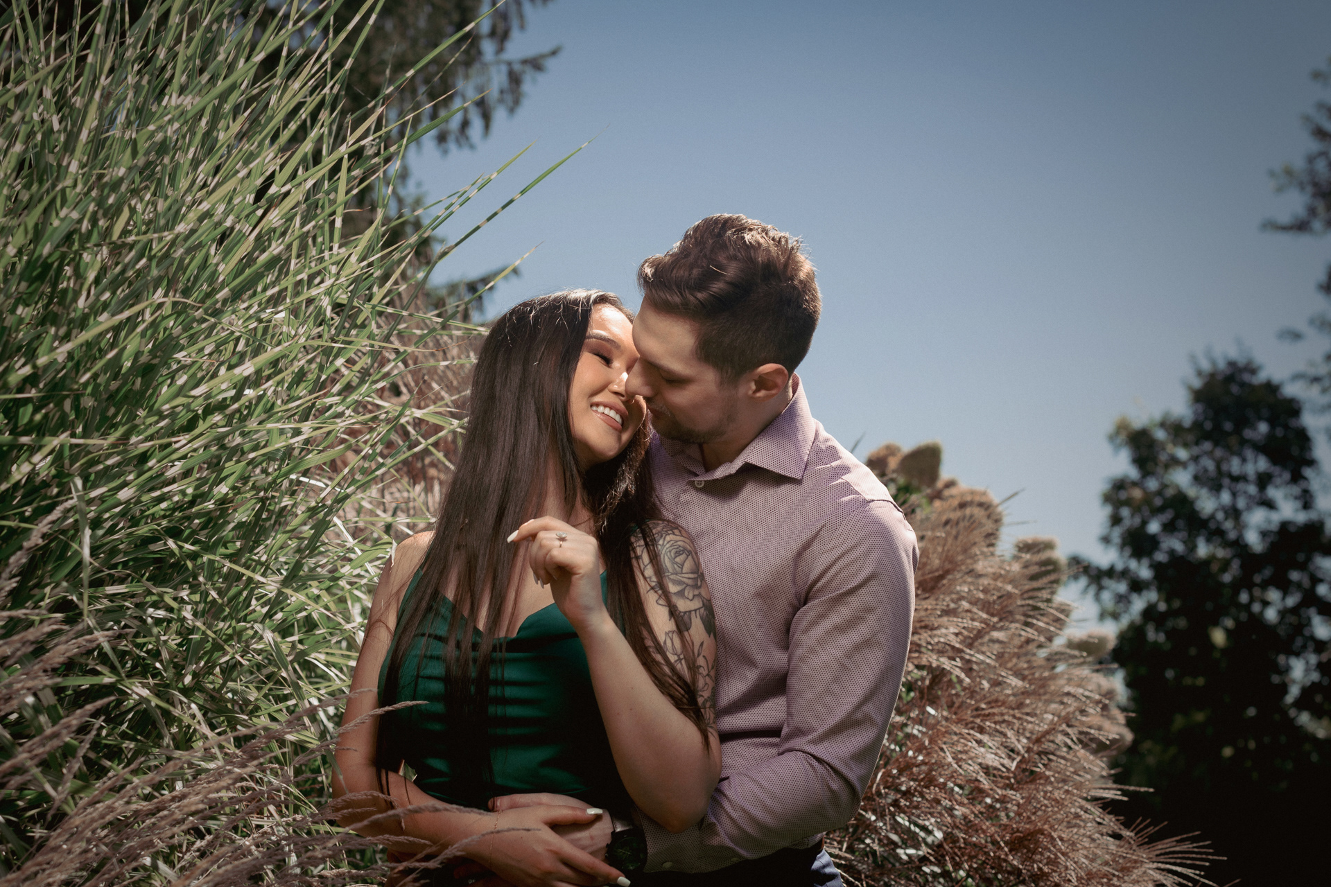 Groom-to-be kissing fiancée’s cheek while she laughs, surrounded by golden grasses.