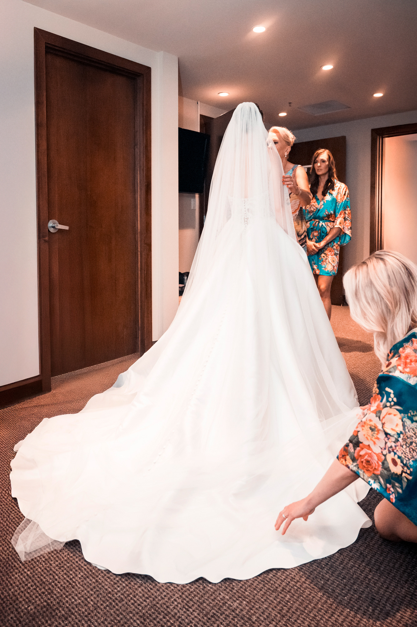 Bridesmaids helping bride adjust gown before walking out.