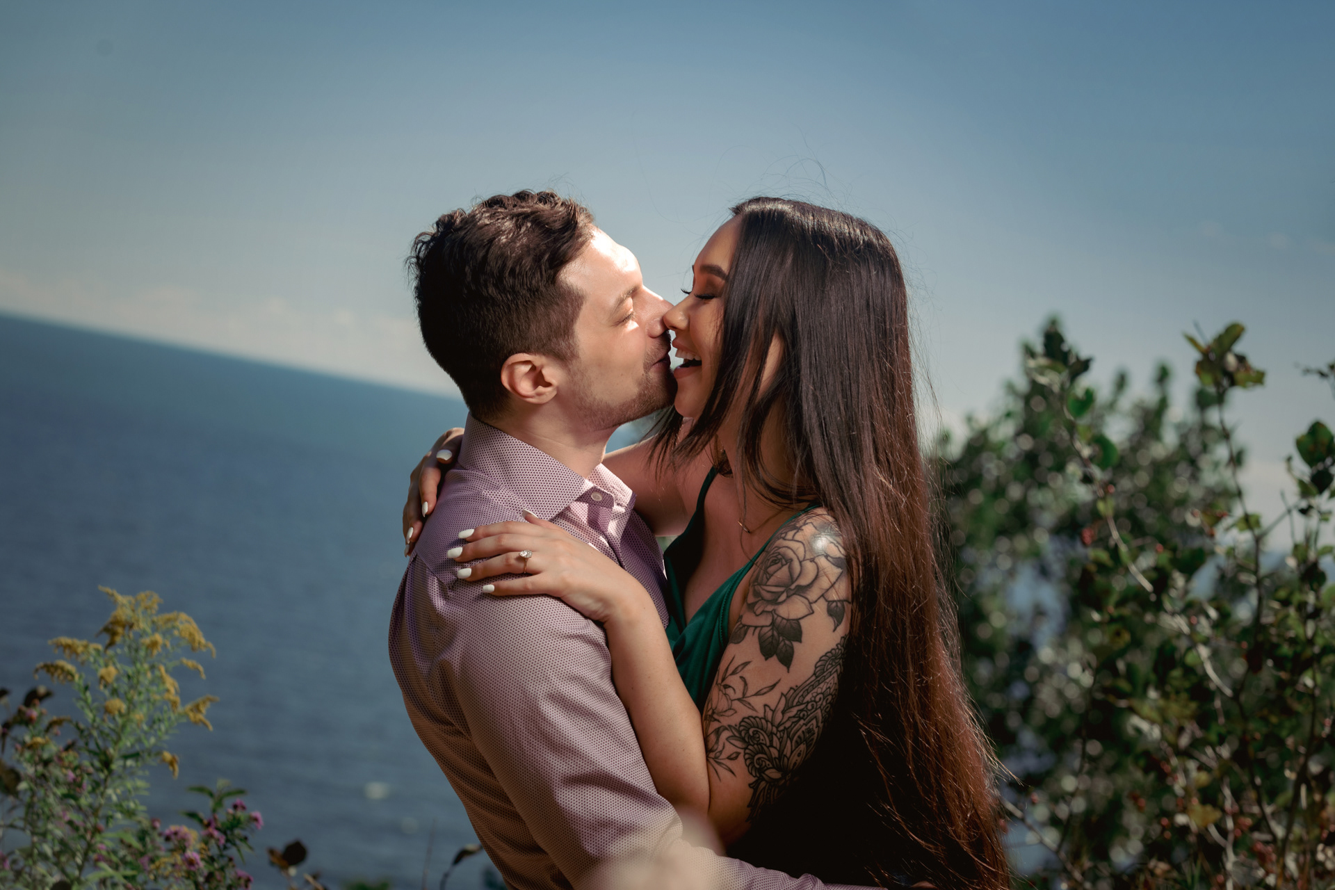 Romantic kiss at the edge of the cliffs overlooking Lake Ontario, fiancée smiling with joy.