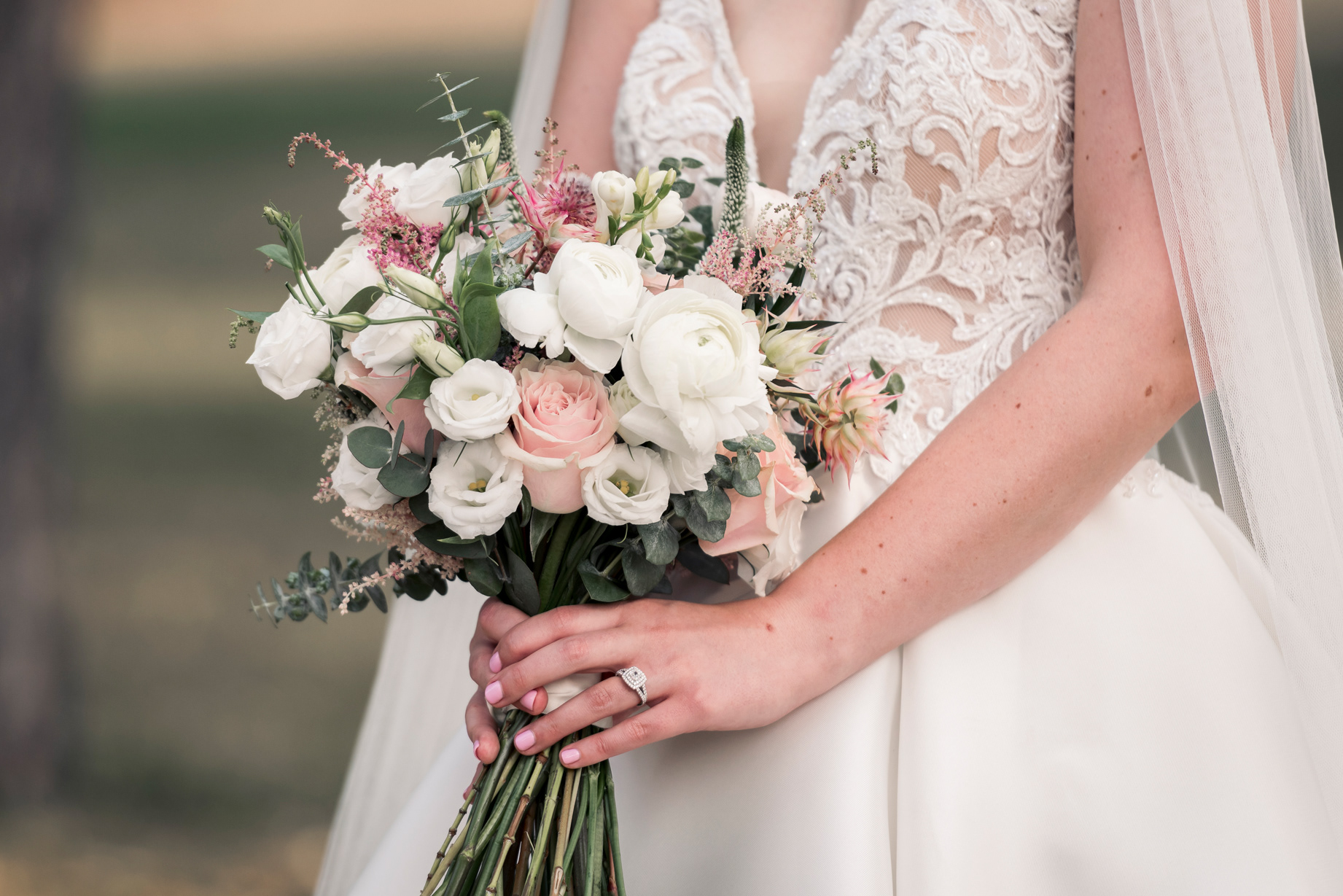 Bride holding pastel wedding bouquet with roses and ranunculus.