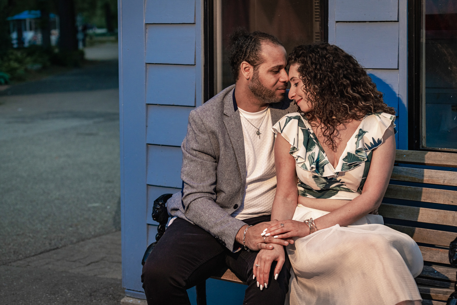 Engaged couple sitting close on a wooden bench, sharing an intimate moment during golden hour engagement shoot.