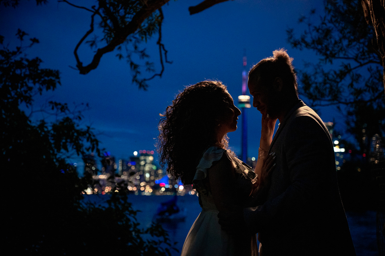 Romantic couple silhouetted at sunset with Toronto city skyline glowing in the background.