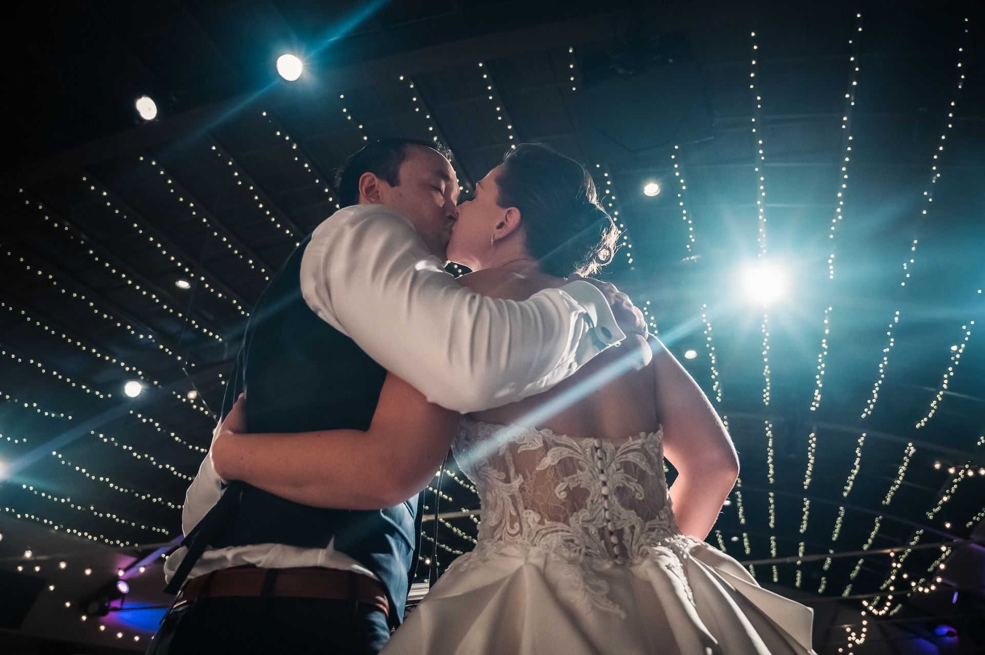 Bride and groom kissing under twinkling string lights at Palais Royale.