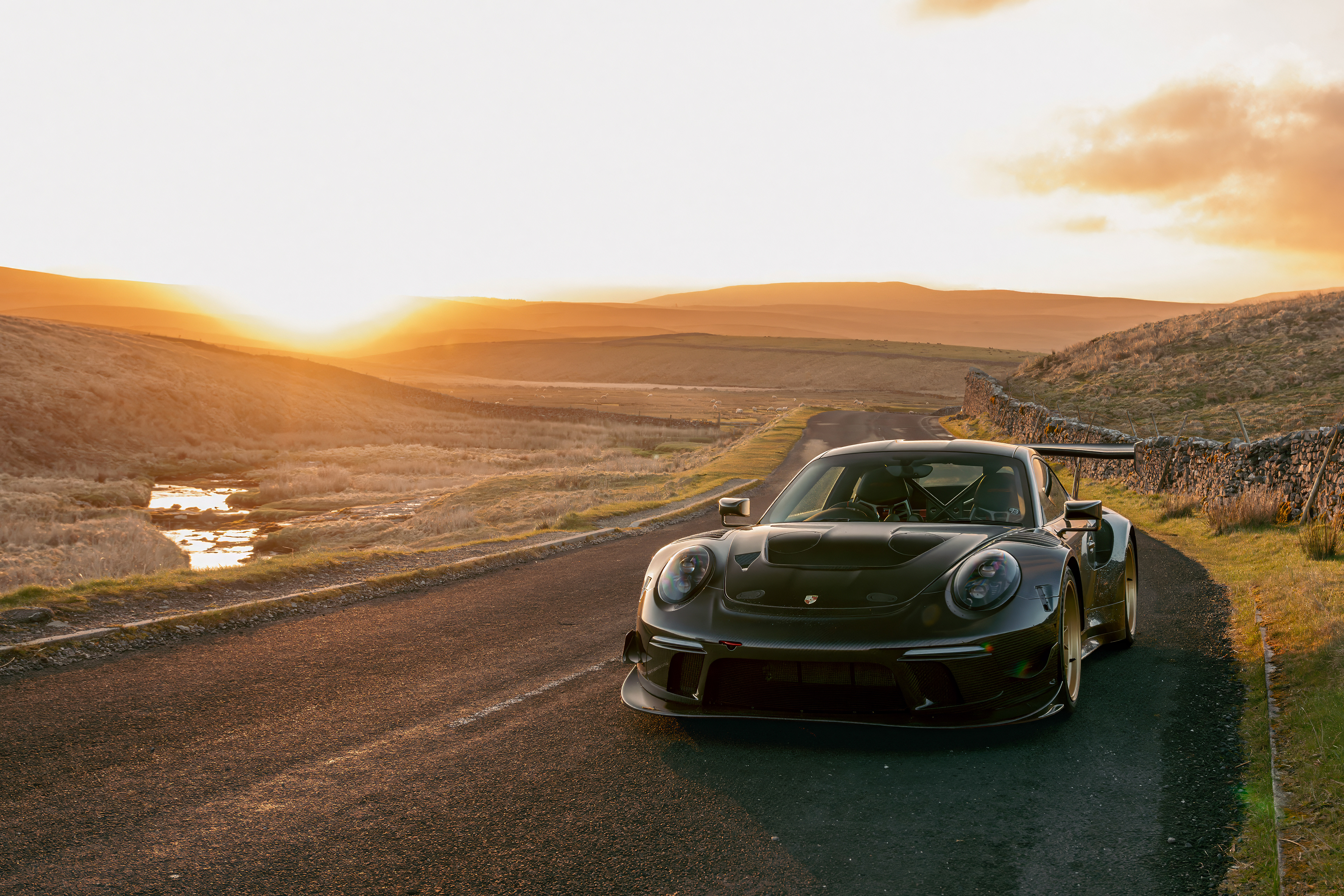 A Porsche 911 RT sports car driving through the Yorkshire Dales at golden hour. The video features aerial drone shots of the Ribblehead Viaduct, close-ups of the car's carbon fiber details, and smooth tracking shots of the vehicle in motion against a vibrant sunset sky.