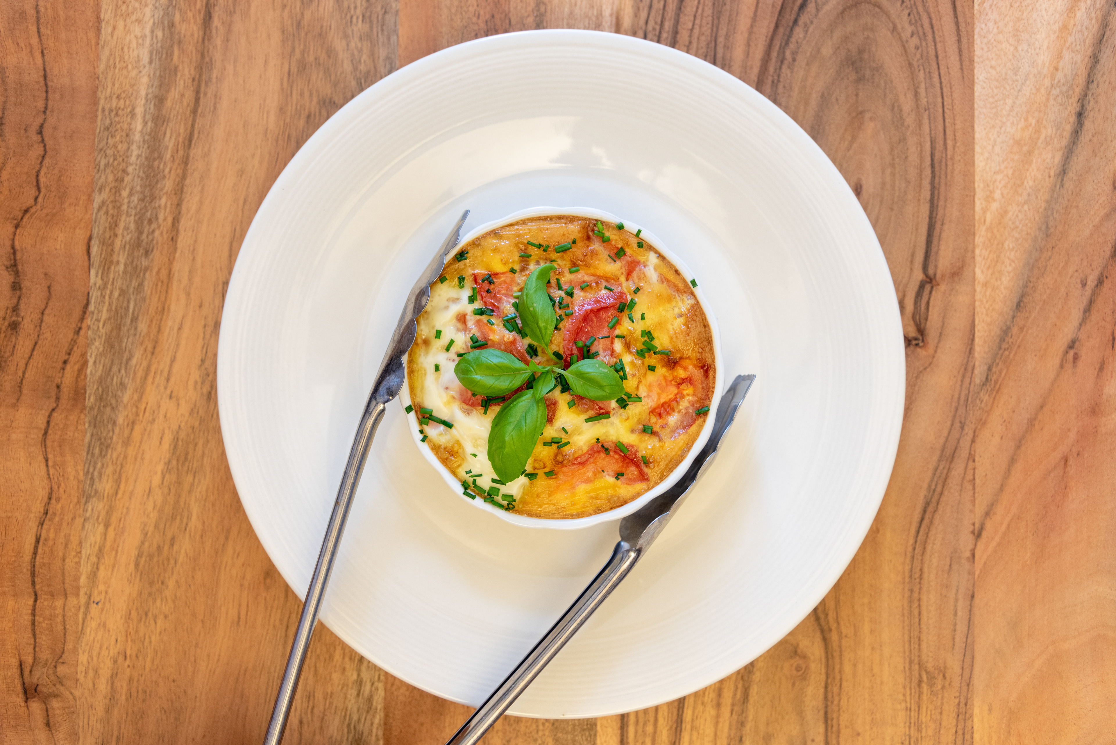 keto low carb tomato and cheese quiche in porcelain in baking pan with tongs
