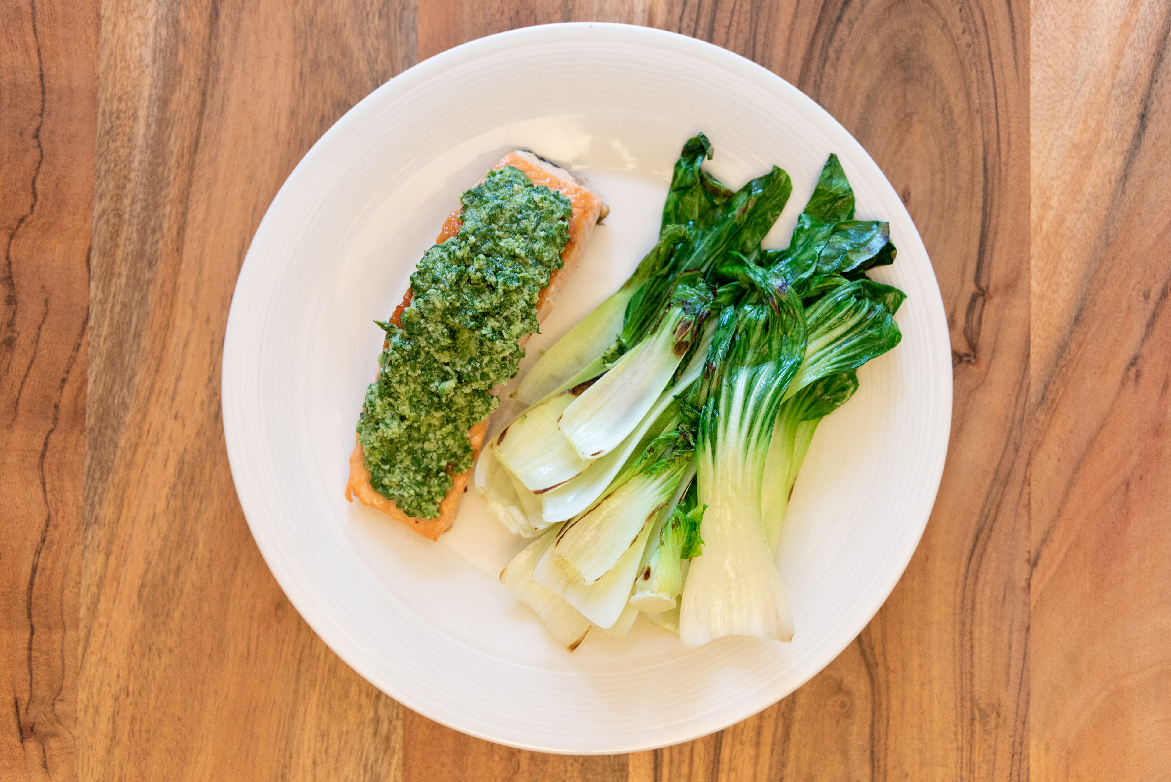 cooked meal of salmon homemade pesto and oak choi on white plate low carb keto