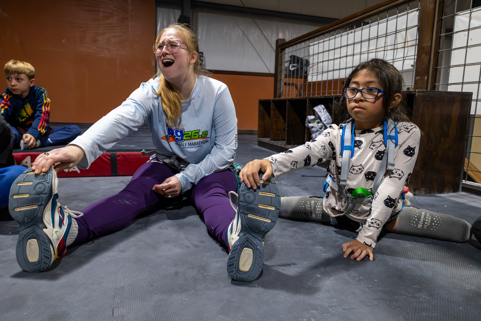 Gabi holds coach KC Ciresi’s shoe while the team does leg stretches before rock climbing at Redpoint Climbing Center on December 3, 2025. When a teammate laughed and asked why Gabi was holding her shoe, KC responded, “We all have our way of doing things, and this is Gabi's way.”