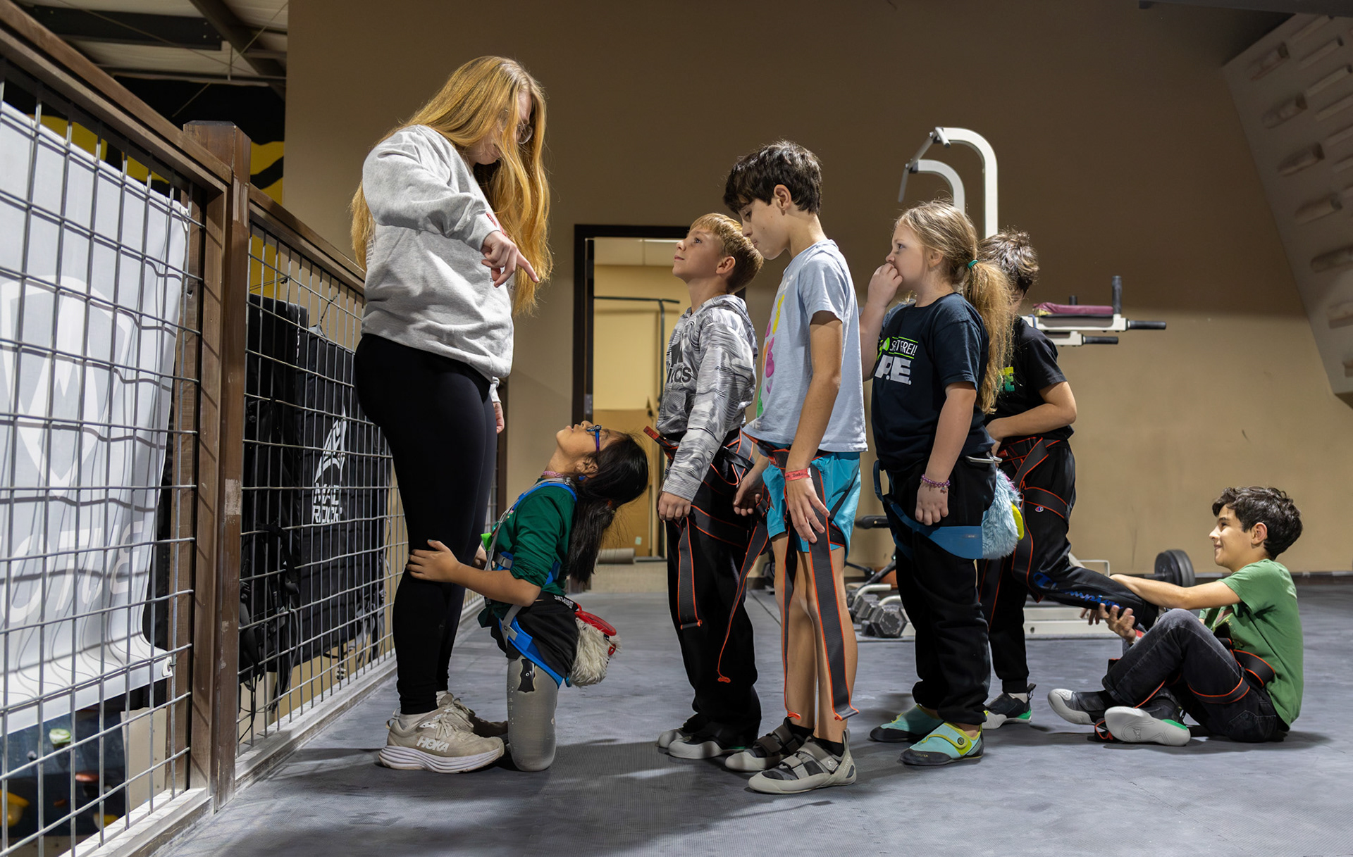 Gabi holds climbing coach KC Ciresi’s legs as Ciresi prepares to assign the first-level team into different climbing routes at Redpoint Climbing Center on Dec. 3, 2025.
