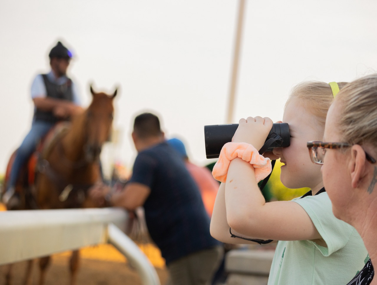 A young girl watches her sister practice riding horses at Keeneland in Lexington, Ky., on Saturday, June 15, 2024. 