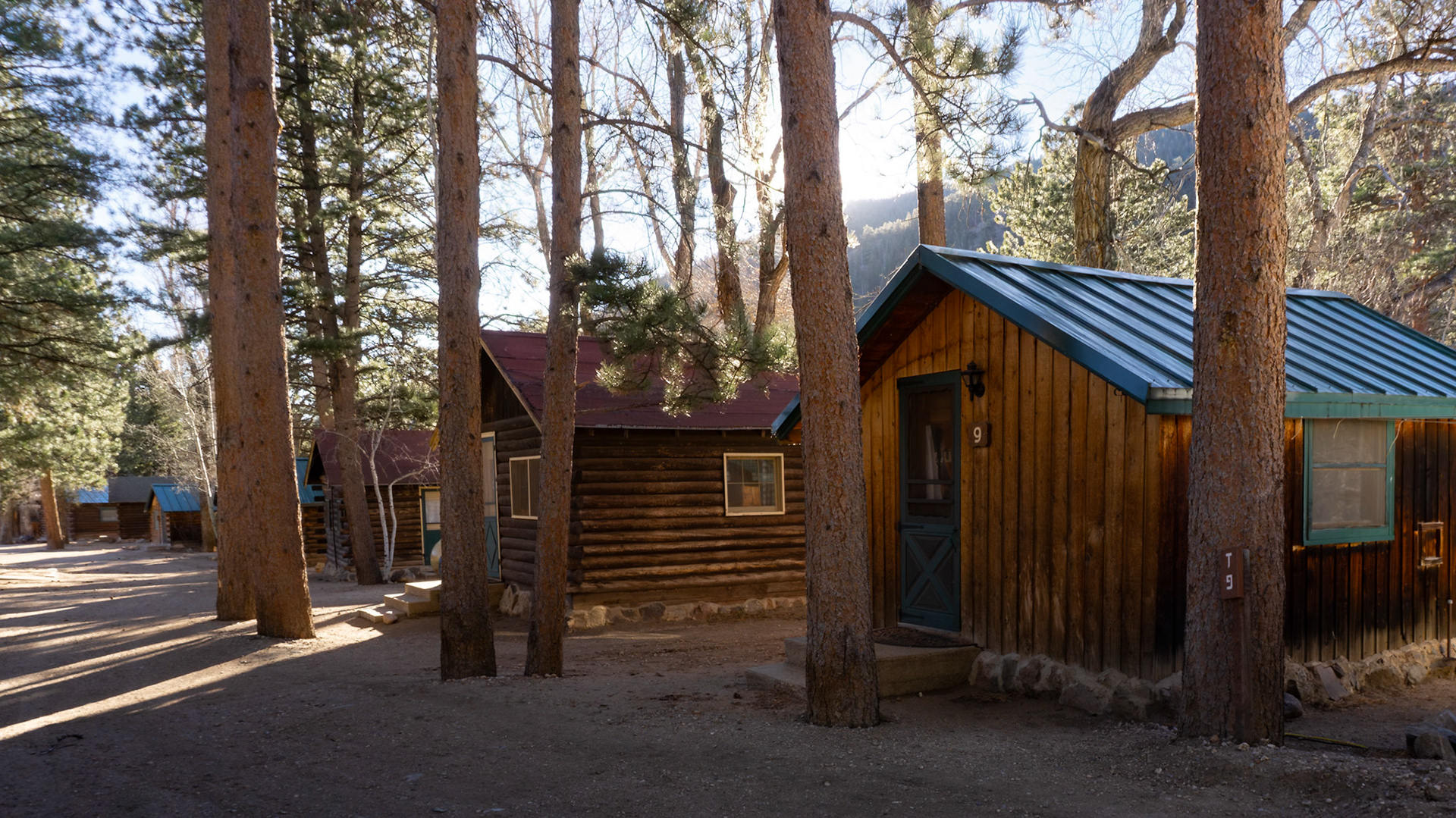 Wide‑angle sunrise view of a Colorado cabin resort with pines, mountains, and warm morning light.