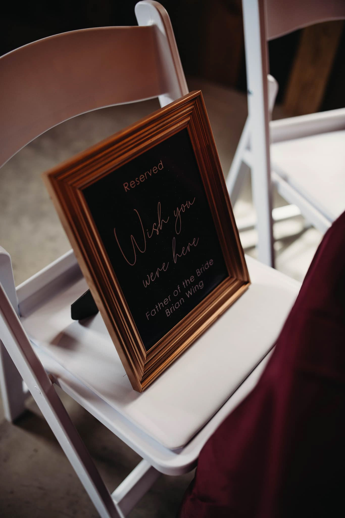 A photo in a gold frame resting on a chair. It reads 'Reserved: Wish you were here. Father of the Bride, Brian Wing.'