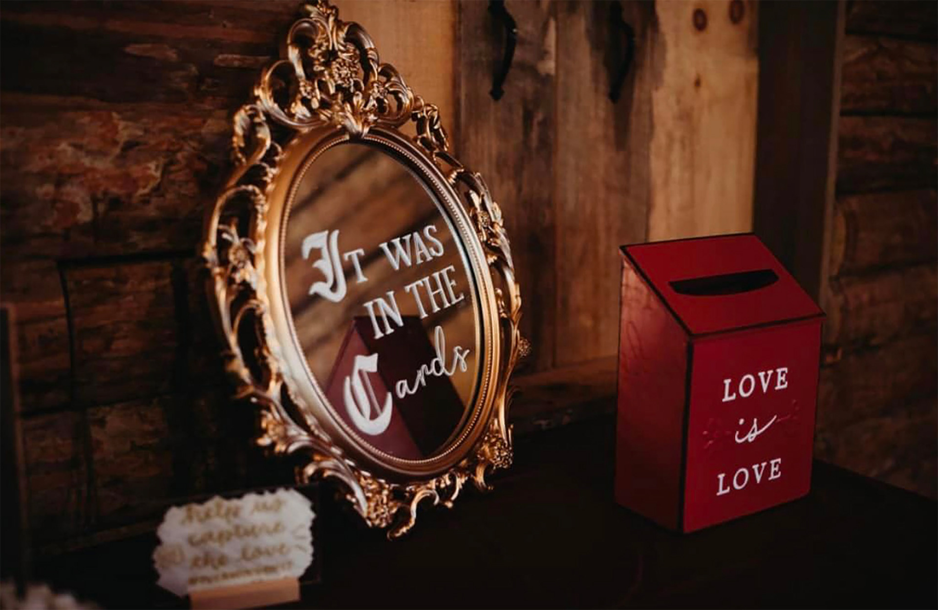 A gold-framed mirror leaned against a log wall that reads 'It was in the cards.'