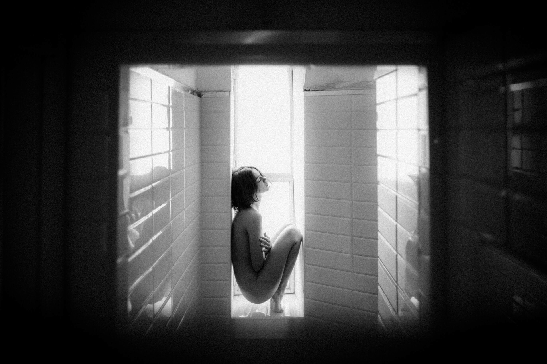 fine art nude woman crouched in shower with strong window light