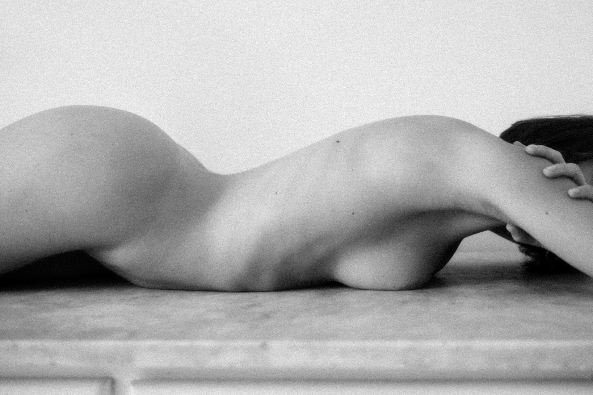 Reclining nude female body in side view with arched back and minimal setting