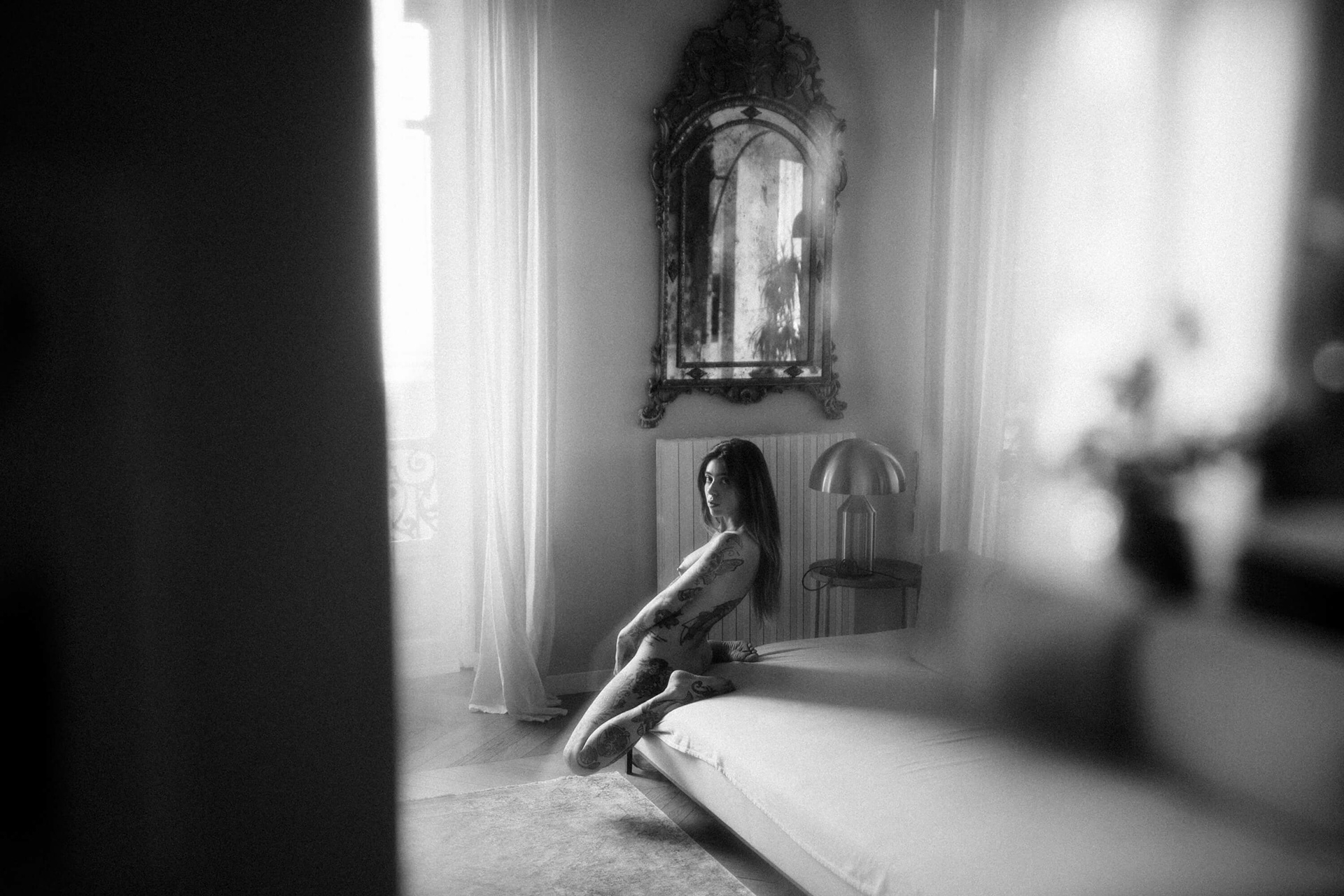 fine art nude woman kneeling on bed seen through soft foreground