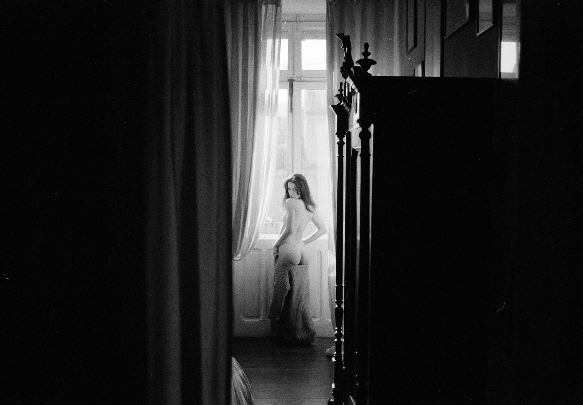 Fine art nude photography of a woman seen from behind near a window framed by curtains