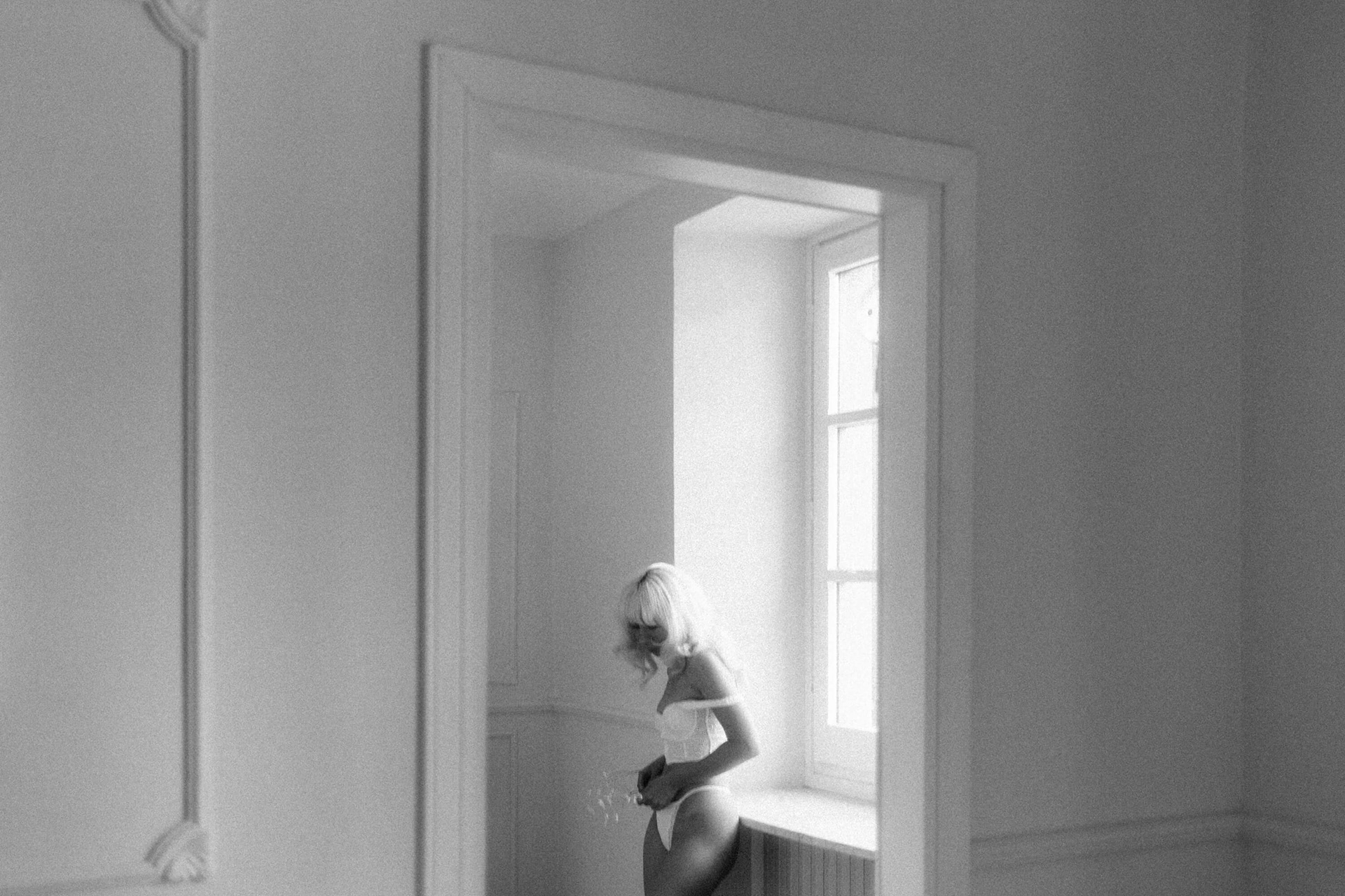 fine art nude woman standing by window in minimalist interior
